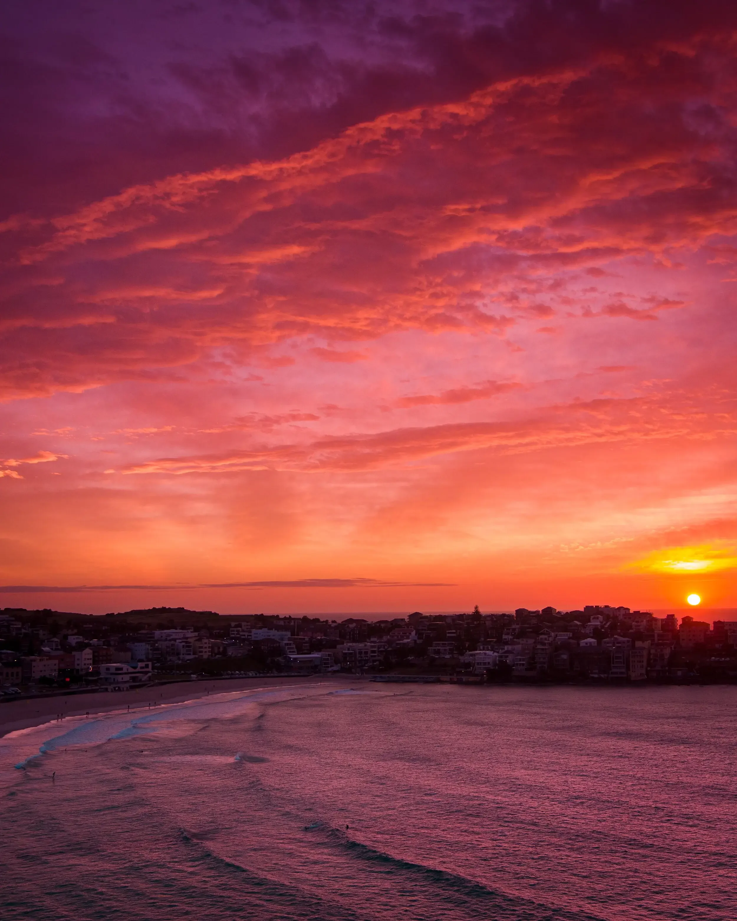 A sunset over a coastal city with pink, purple, and orange clouds in the sky