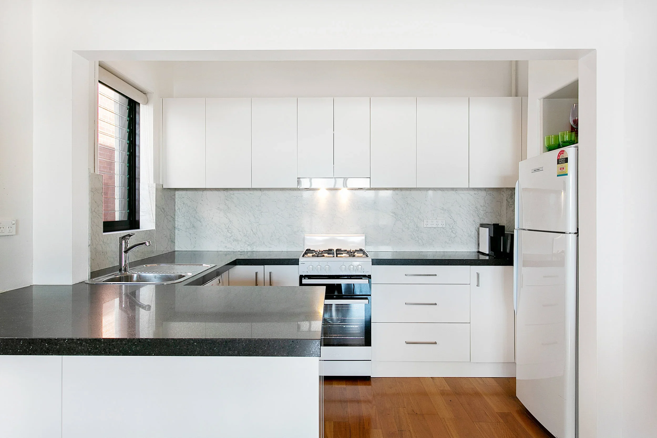 Modern kitchen with white cabinets, black countertops, marble backsplash, stainless steel stove, and white refrigerator.
