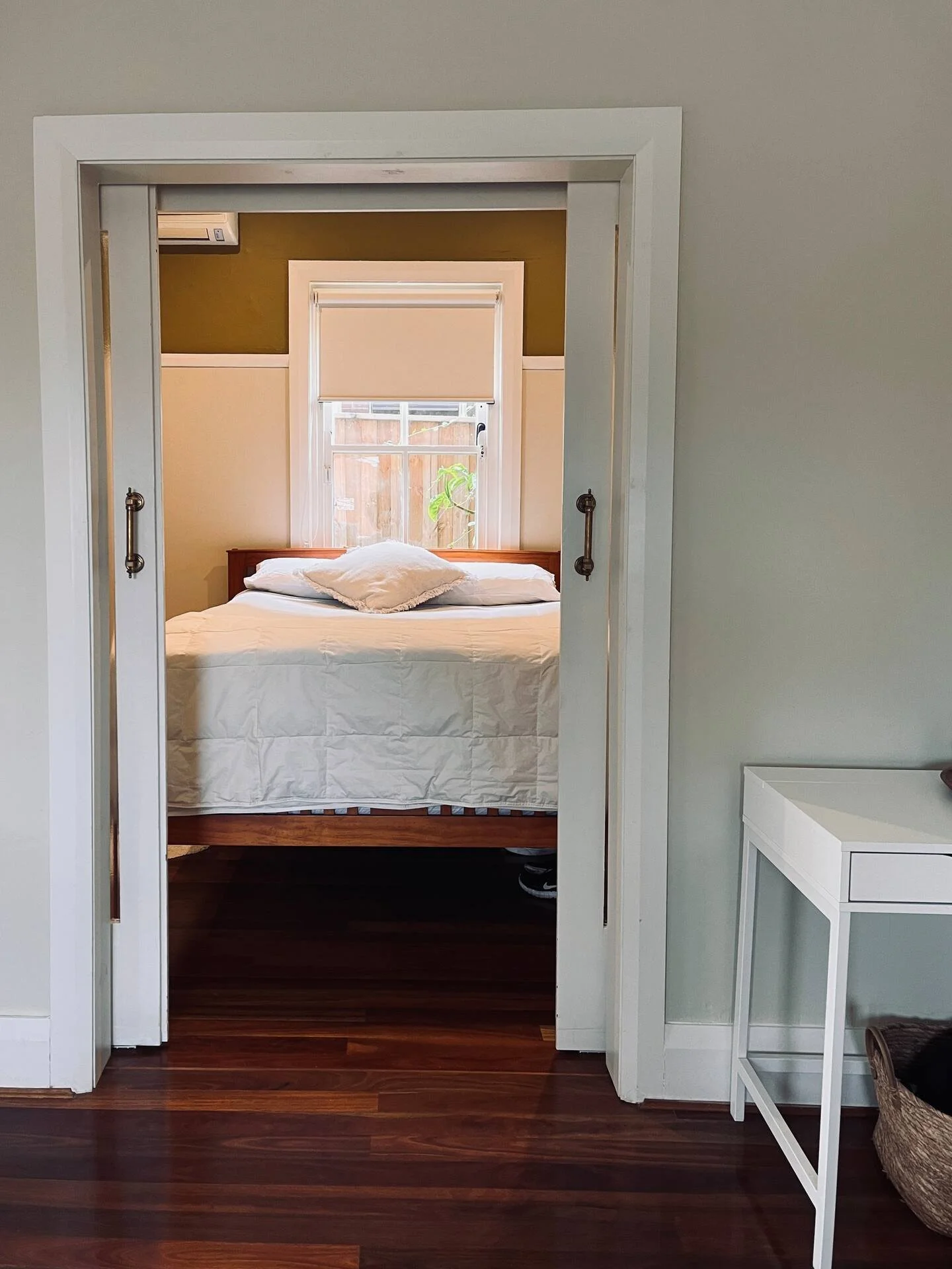 View through a doorway into a bedroom with a bed, a window, and a potted plant outside.
