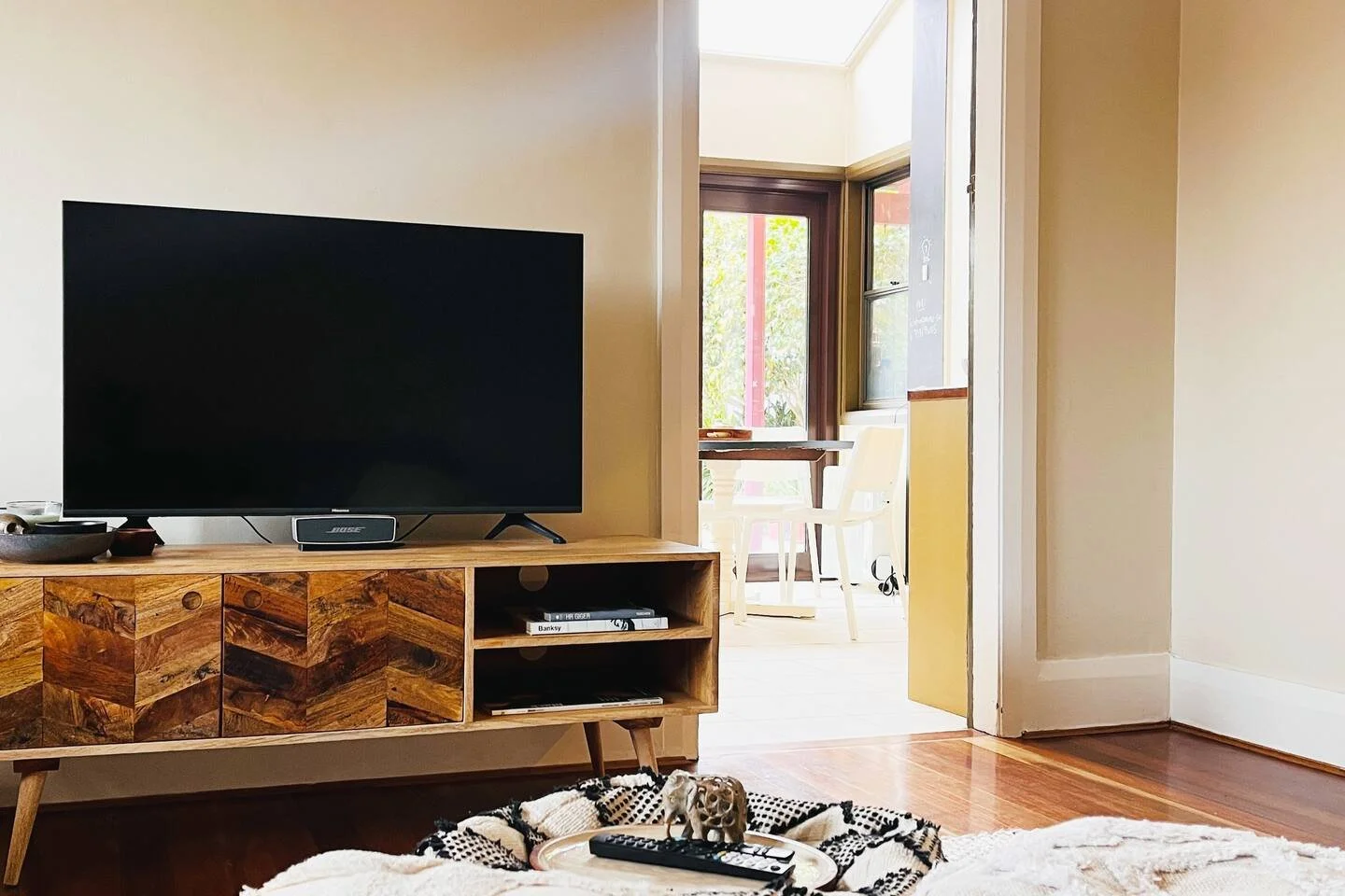Living room with flat-screen TV on wooden TV stand, and a small dog toy on a remote control and a patterned hat on a tray on the rug in front.