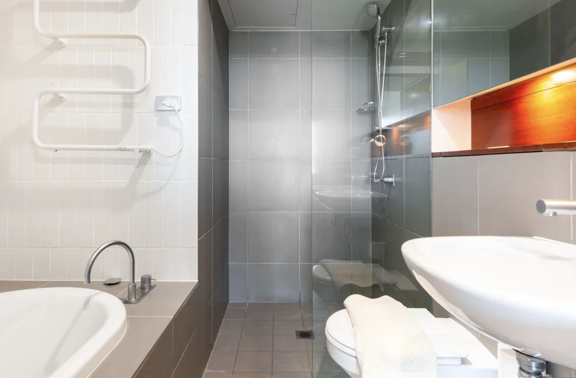 A modern bathroom with a walk-in shower, a white sink with a towel, a toilet, and a heated towel rack on the wall.