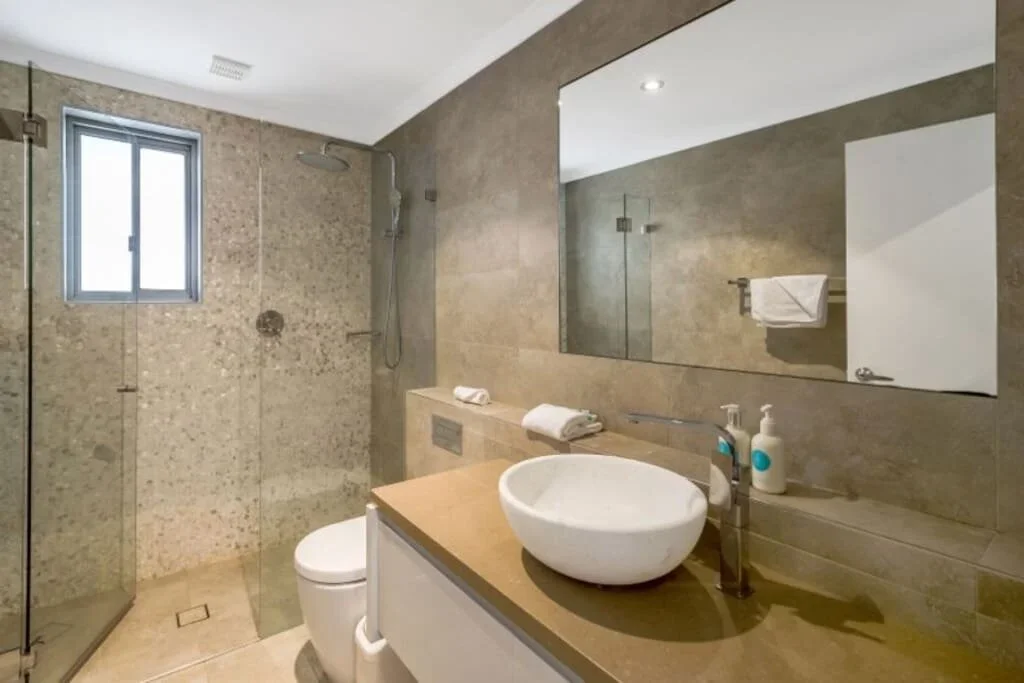 Modern bathroom with a walk-in shower, a large mirror, a vessel sink, and a window in neutral tones.