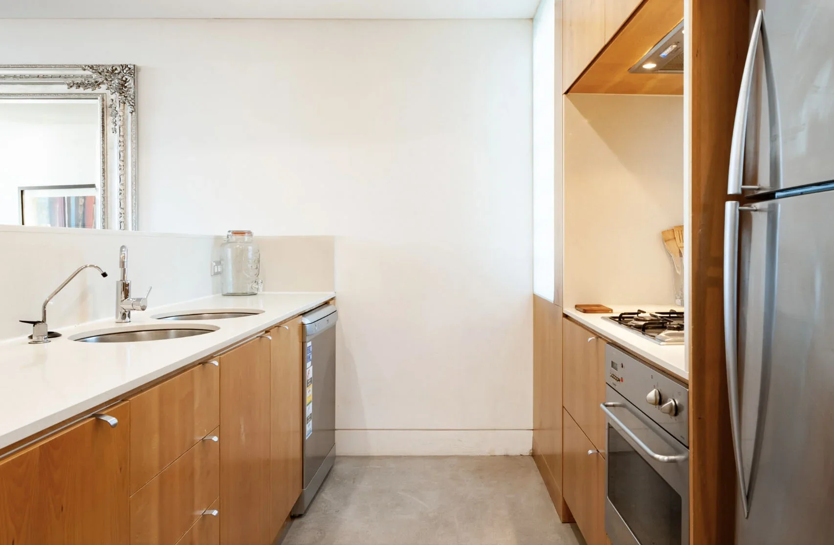 Modern kitchen with white countertops, wooden cabinets, stainless steel appliances, a double sink, and a refrigerator.