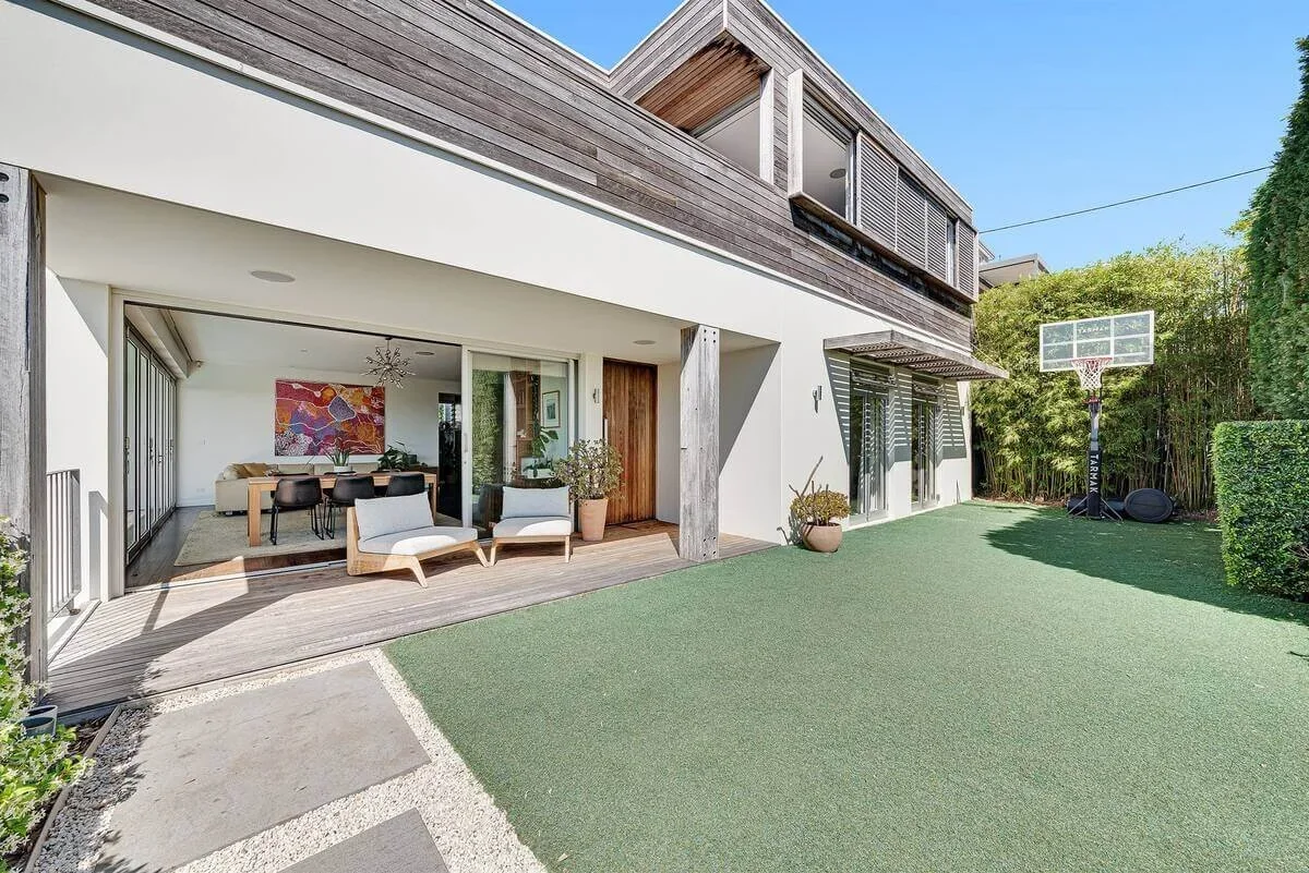 Modern house with a spacious backyard featuring a basketball hoop and an outdoor deck with seating.