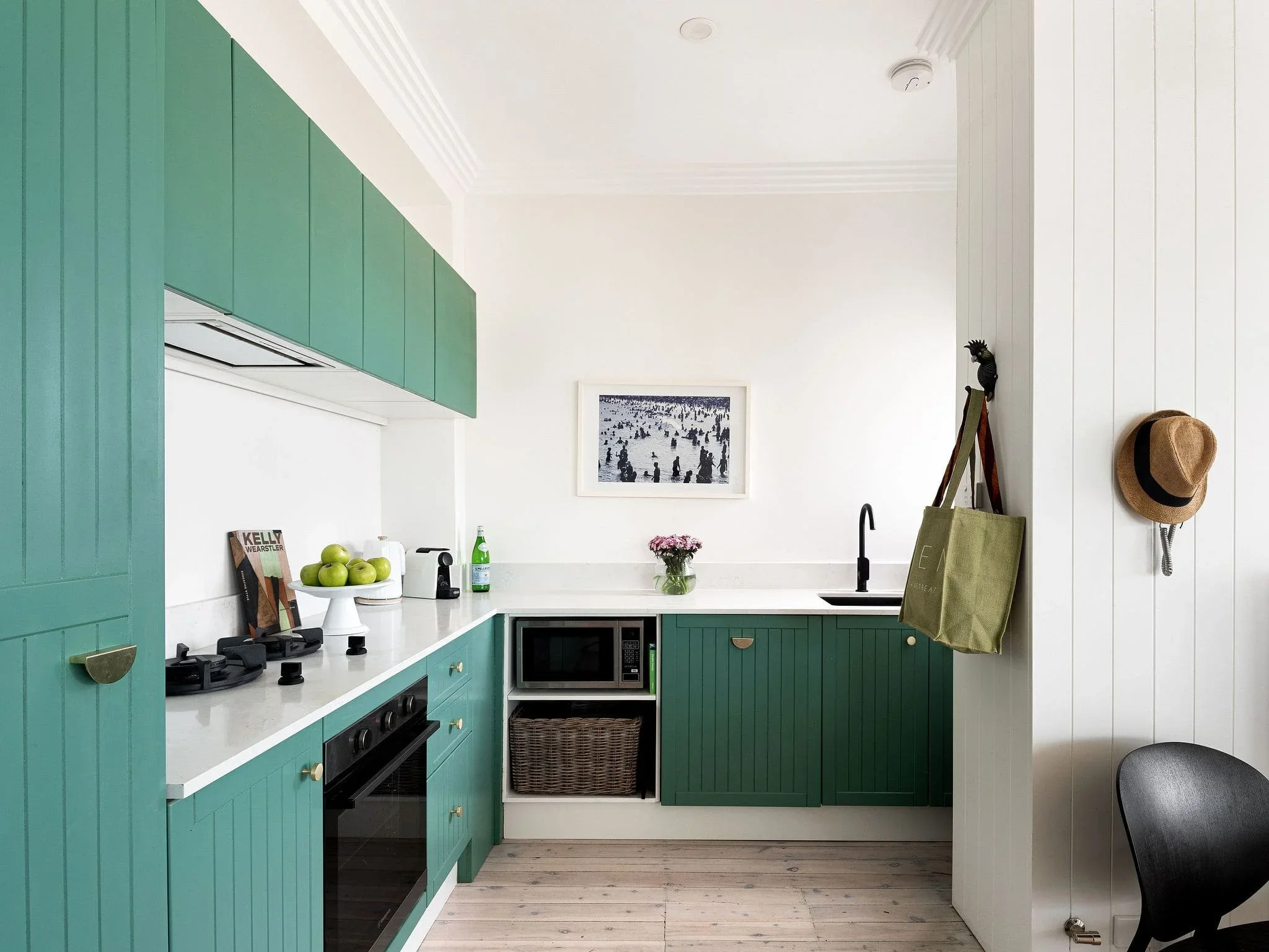Kitchen with green cabinets, white countertop, black stove, microwave, artwork, green apple bowl, and hat on wall