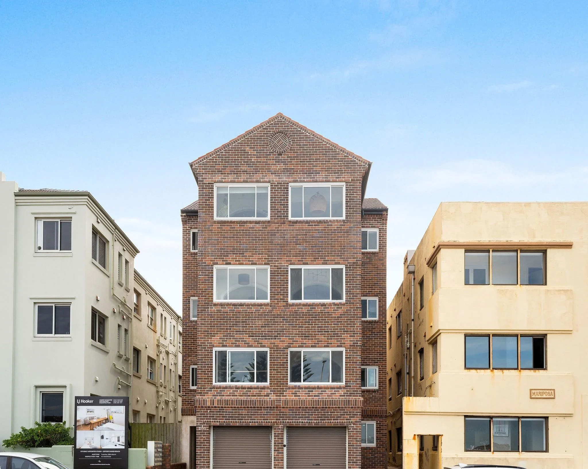 Multi-story residential building with brick facade between two other buildings, one white and one yellow, under a blue sky.