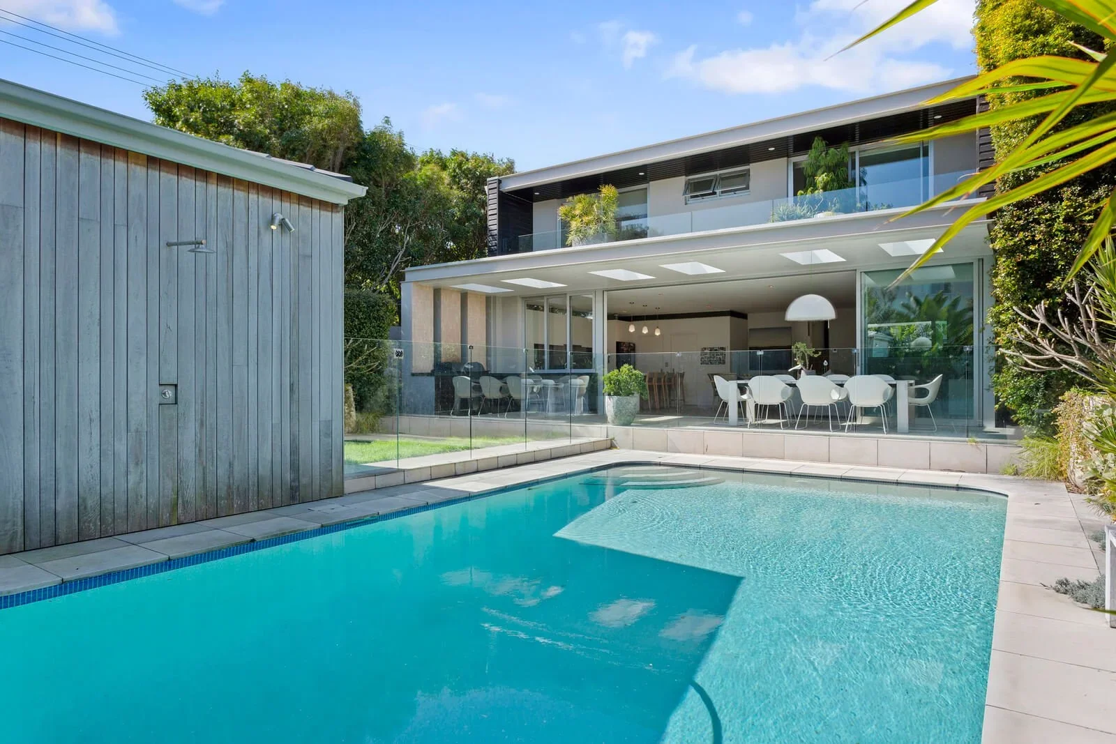 Modern house with open outdoor living space, glass railing, and swimming pool in the backyard on a sunny day.