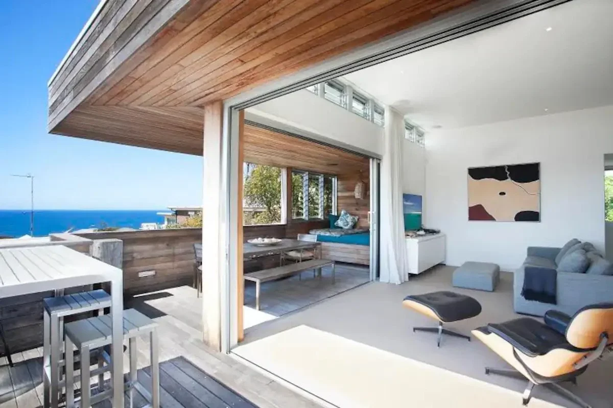 Living room with sliding glass doors opening to a balcony with ocean view, modern furniture including a chair and sofa, and wall art.