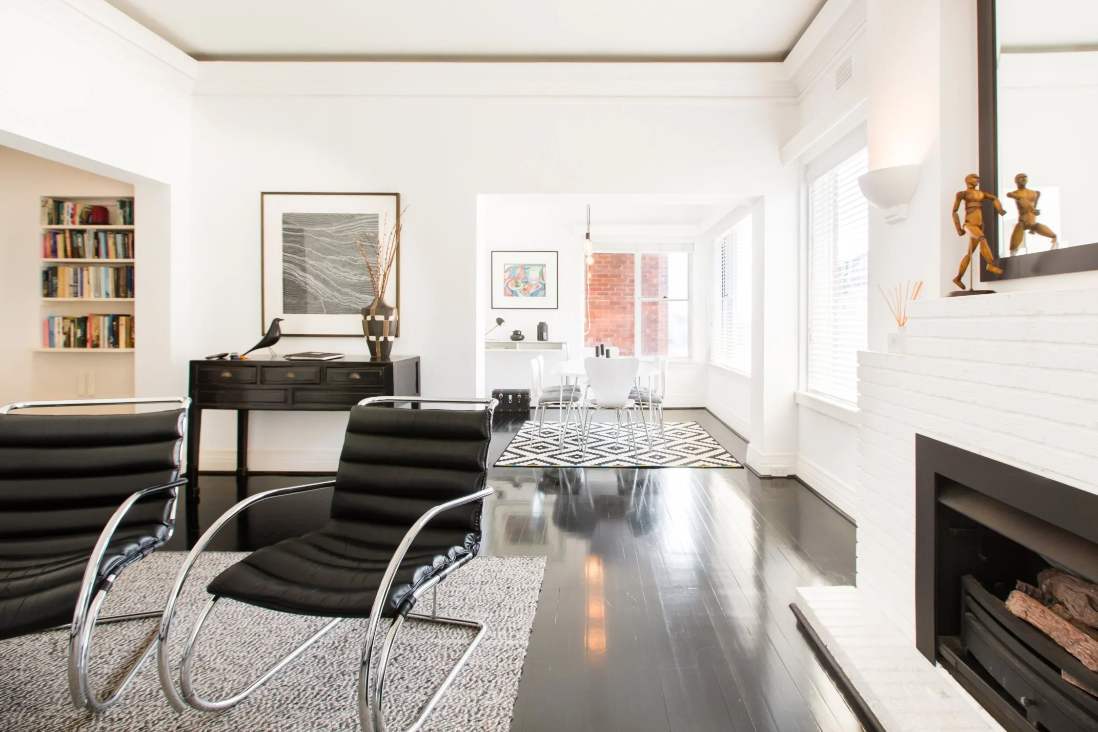 Bright living room with black leather chairs, a fireplace, a bookshelf, and a dining area in the background.