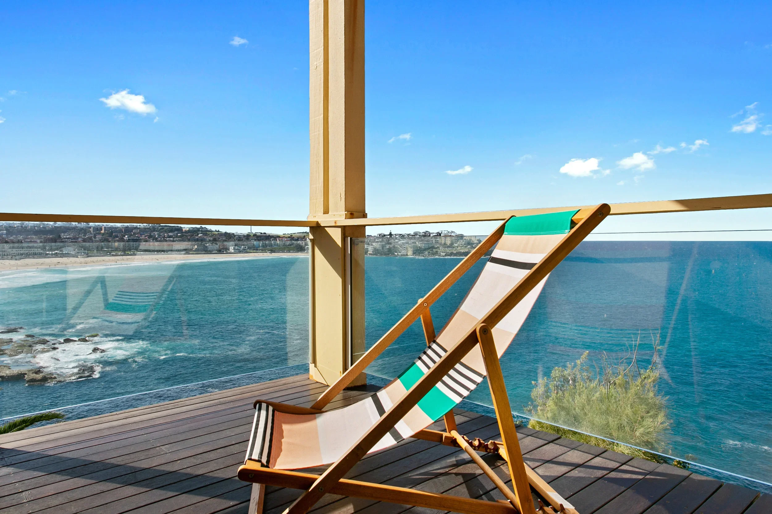 A lounge chair on a balcony overlooking the ocean, with a distant shoreline and a clear blue sky.