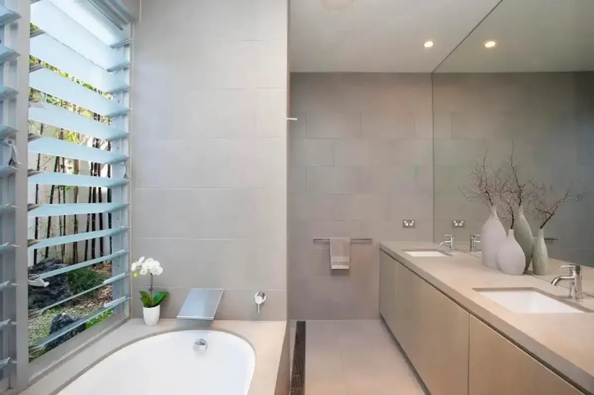 Modern bathroom with a bathtub, a large mirror, and a double vanity with three white vases decorated with branches.