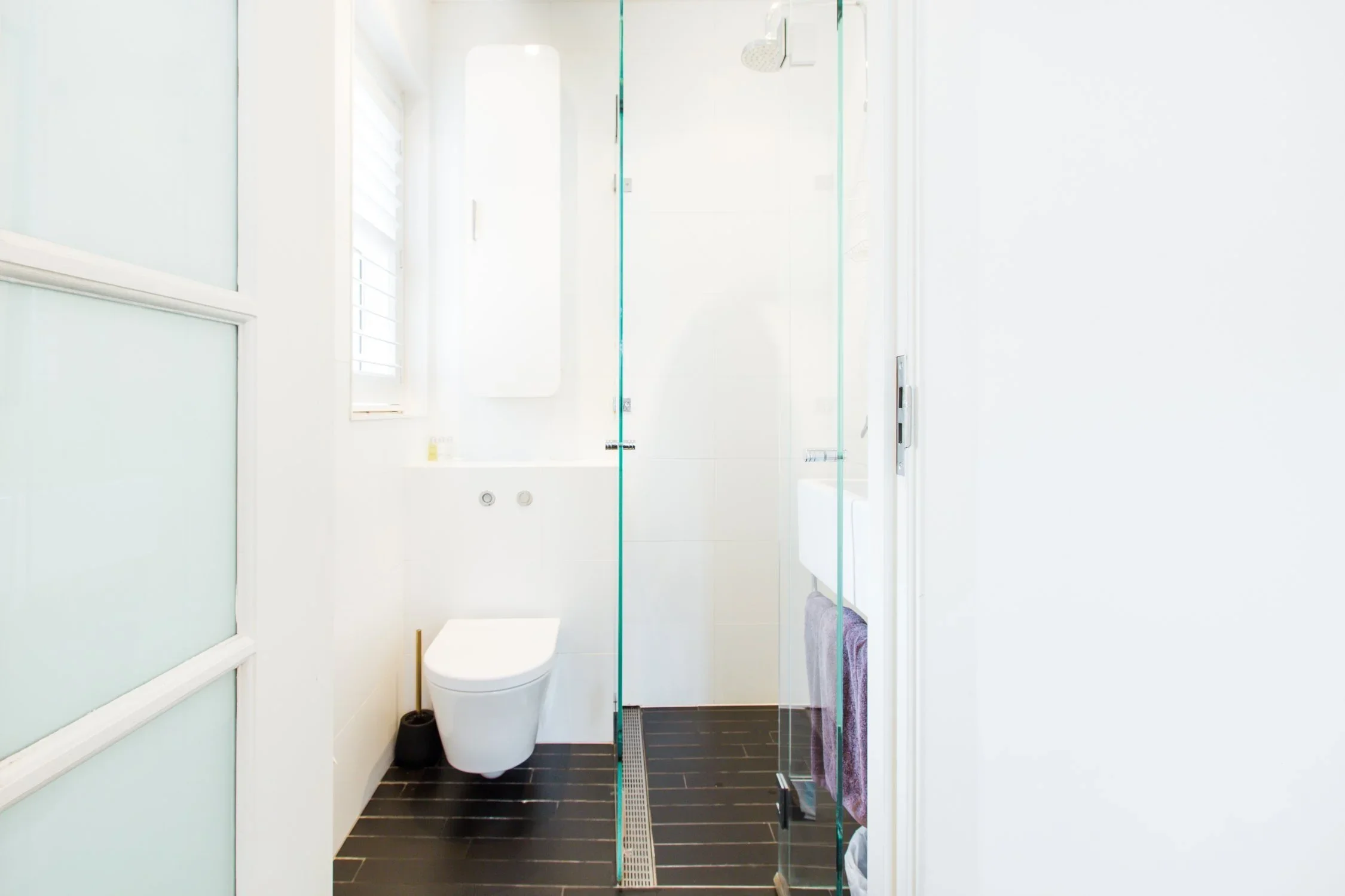 Modern bathroom with a white toilet, a glass shower enclosure, and a small window with white blinds.