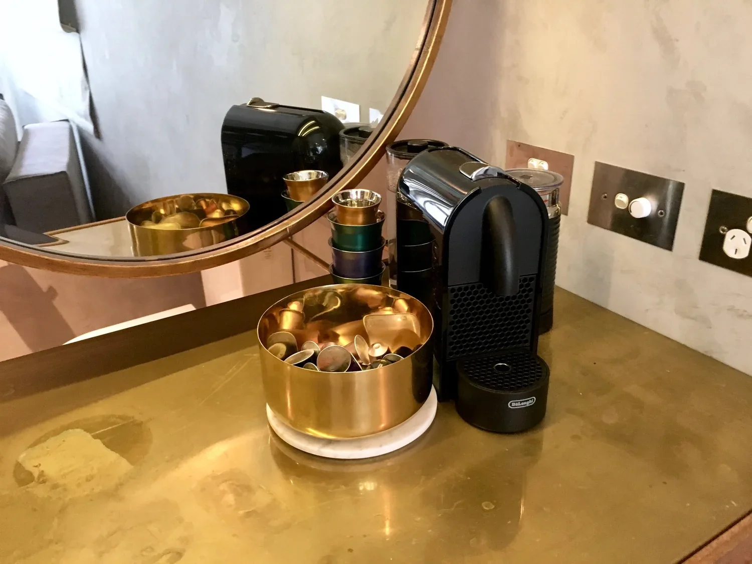 A Keurig coffee machine on a gold-colored countertop next to a golden bowl of coffee pods.
