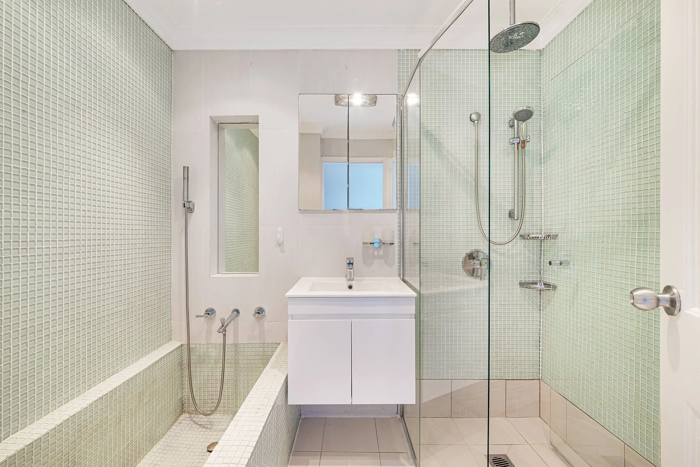 Modern bathroom with a walk-in shower, wall-mounted sink, mirrored medicine cabinet, and tiled walls and floor.