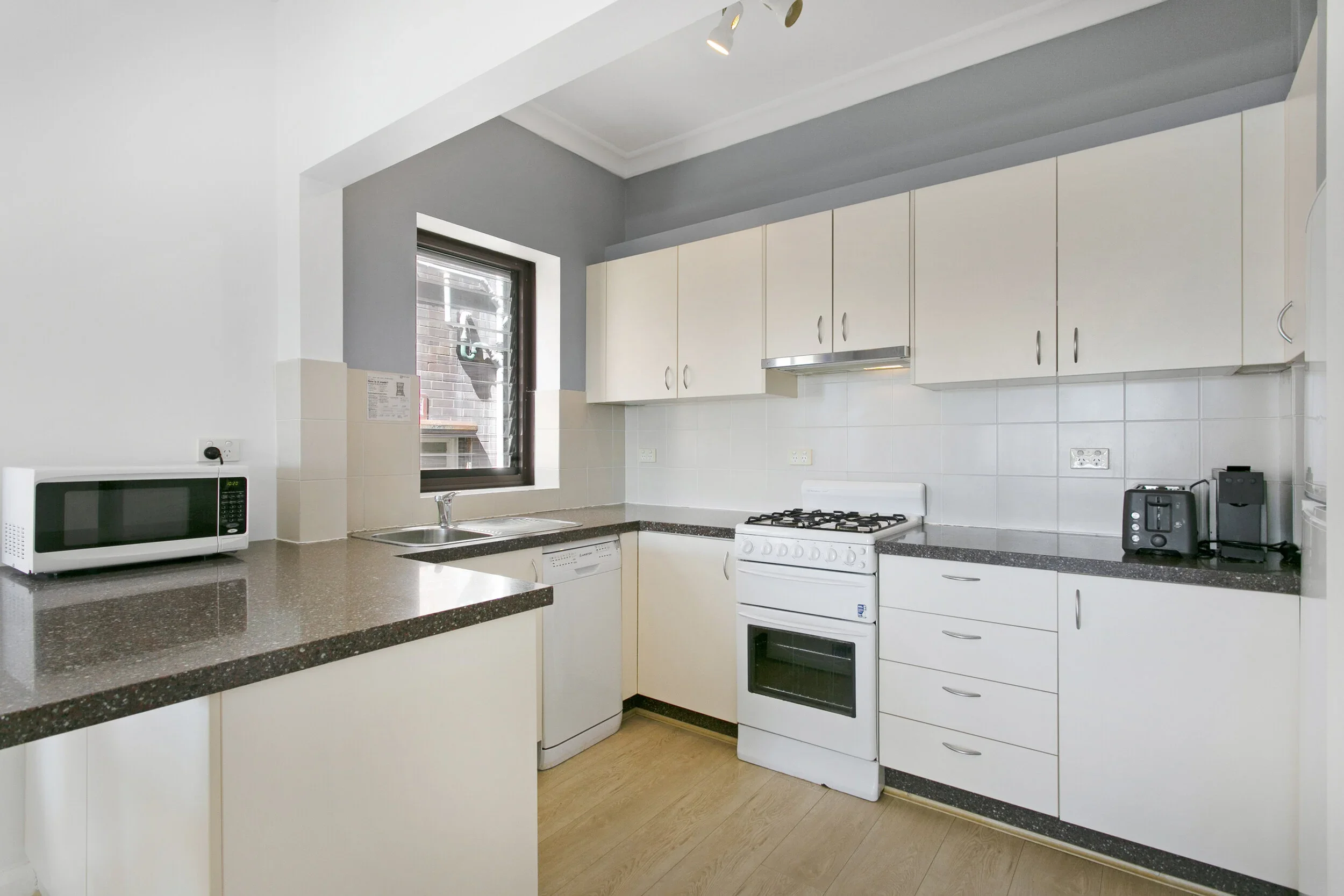 Kitchen with white cabinets, a window, a microwave, a dishwasher, a stove, a toaster, and a coffee machine.