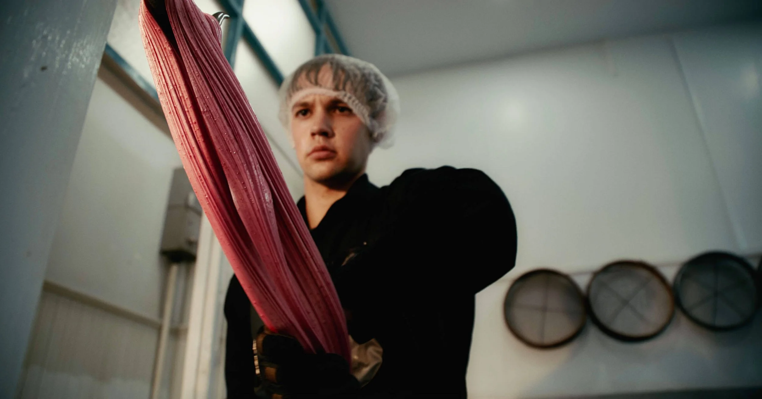 A man wearing a hairnet and black uniform inspecting a large stack of pink meat trays in a meat processing or packaging facility.