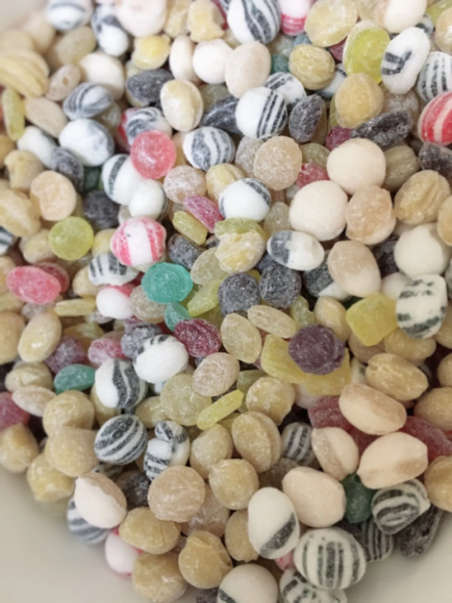 Close-up of colorful round candies with various patterns and sugar coating in a bowl.