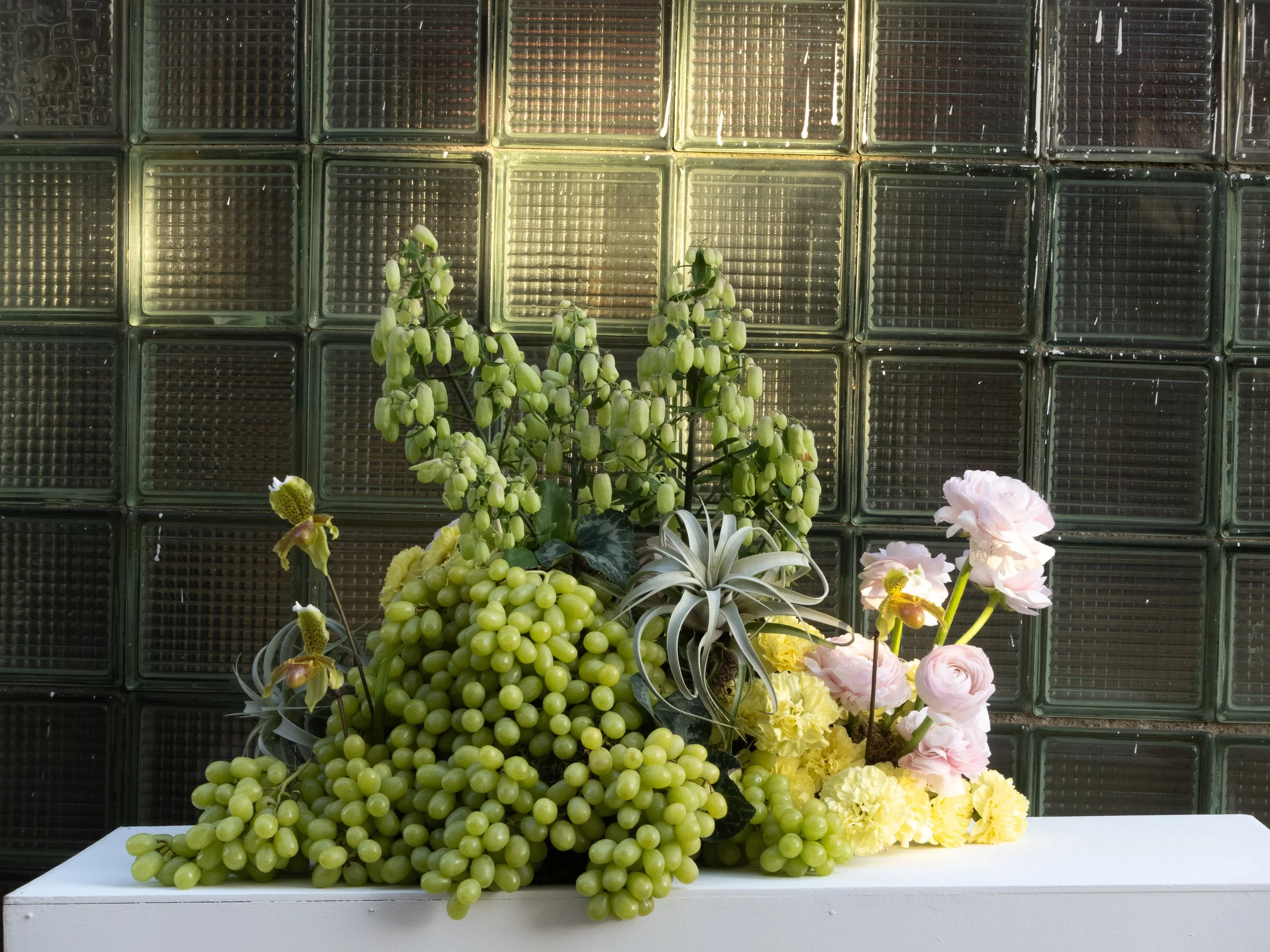 A floral arrangement with green grapes, flowering plants, and a pink rose, displayed in an industrial area in Berlin