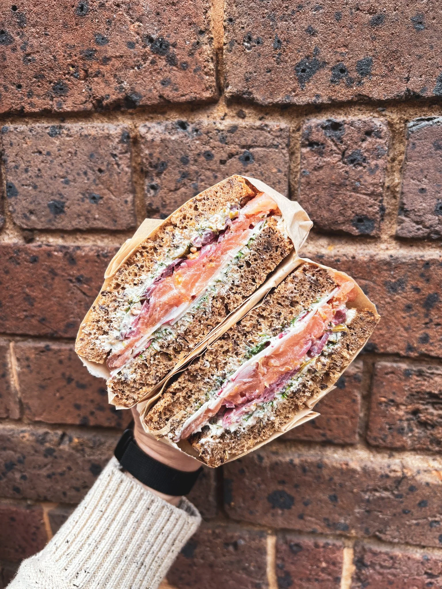 A cut sandwich with smoked salmon, cream cheese, and vegetables in front of a brick wall.