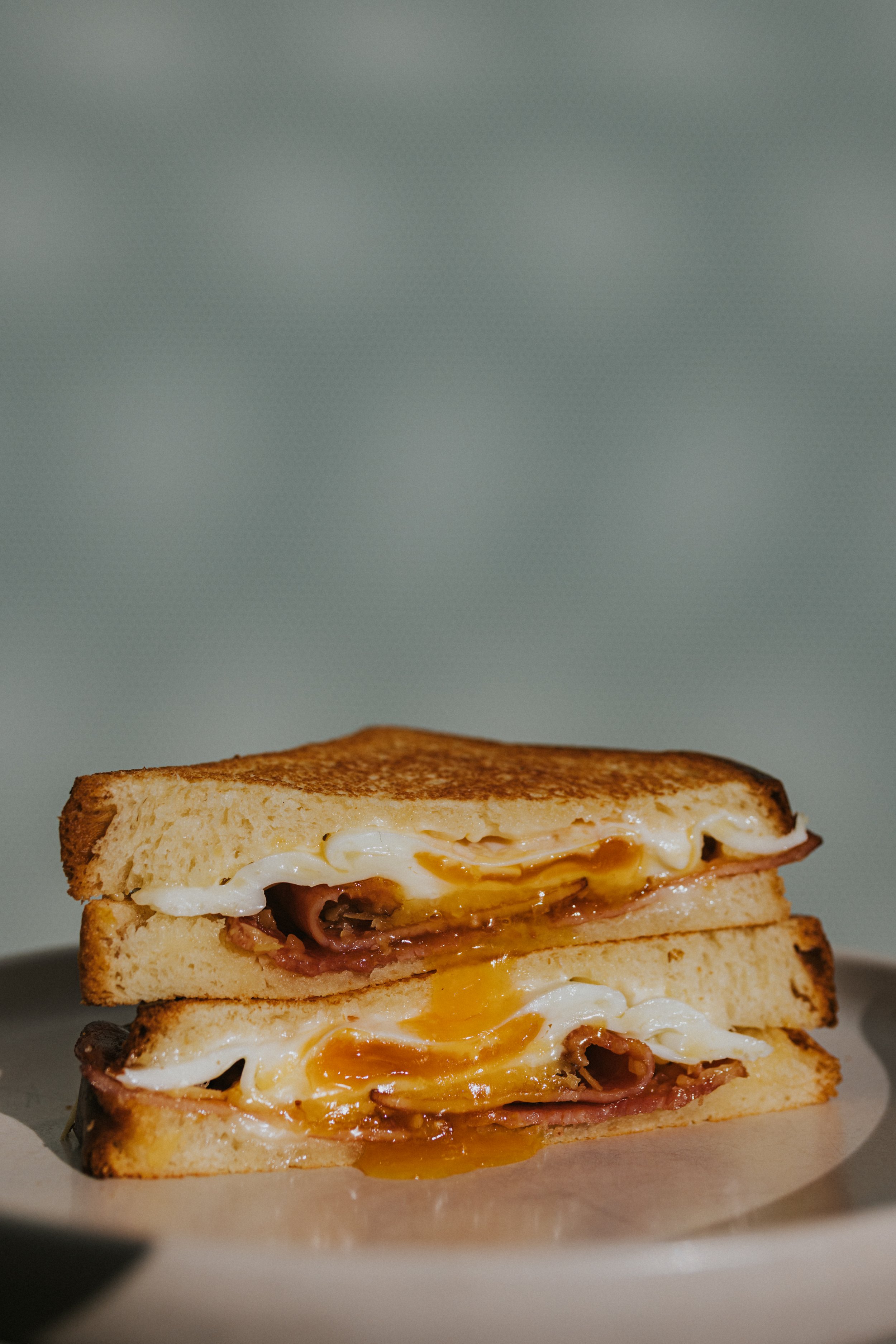 Close-up of a breakfast sandwich with fried eggs, ham, and melted cheese between toasted bread slices.