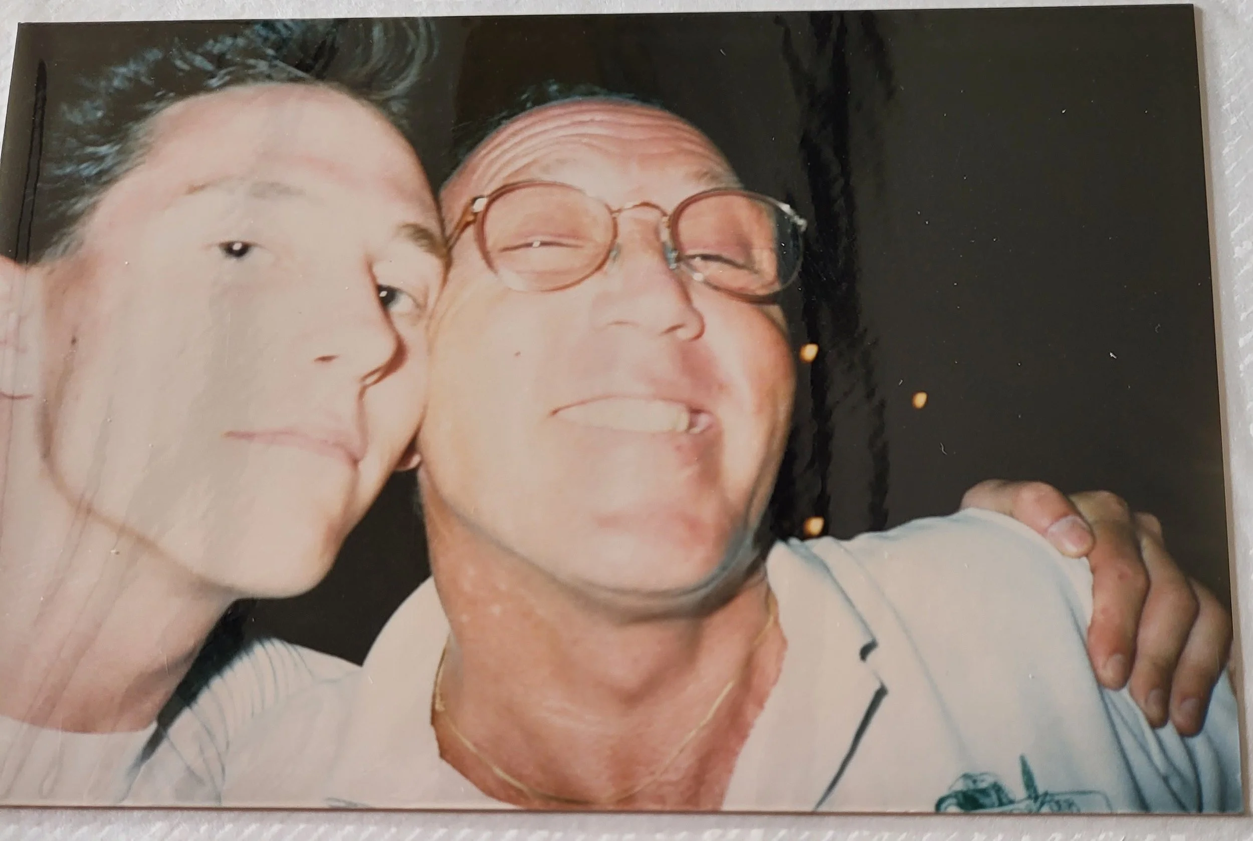 A woman and a man taking a close-up selfie, both smiling with the woman's head resting against the man's cheek, and the man's arm around her shoulder.