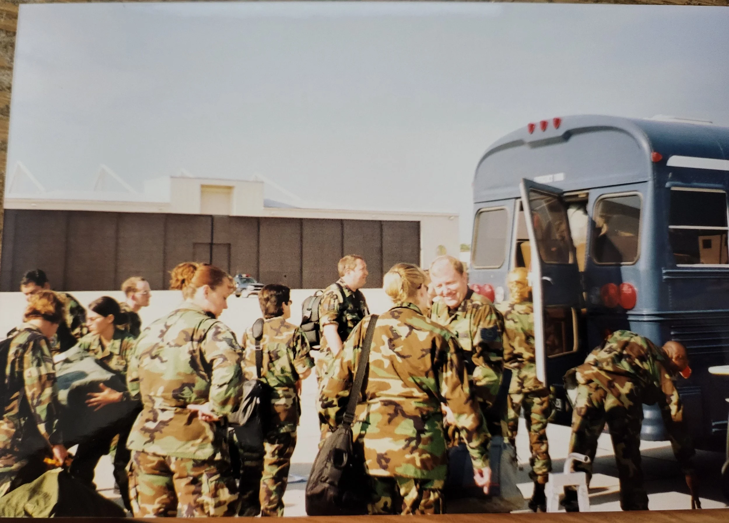 Group of soldiers in camouflage uniforms boarding a blue bus at an outdoor setting, possibly an airfield or military base.