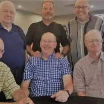 Five men, three standing in back and two sitting in front, pose for a group photo indoors. All are casually dressed.