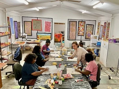 People sitting at a long table working on art projects in an art class room with colorful artworks on the wall.