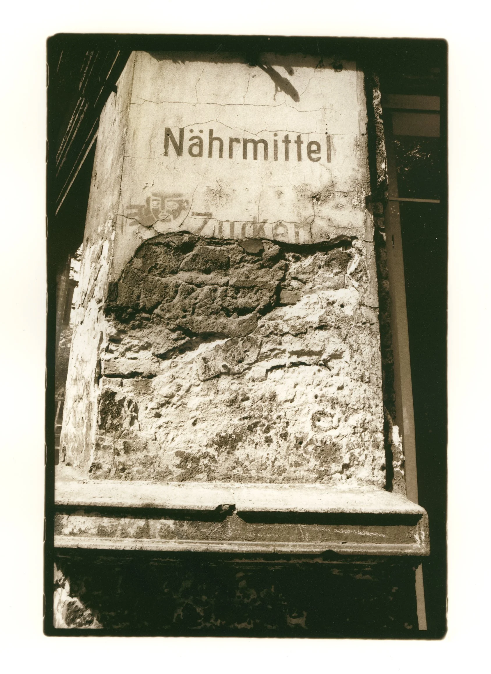 A weathered sign on a brick wall with the word "Nahrmittel" written on it, in front of a textured surface with cracks and old paint.