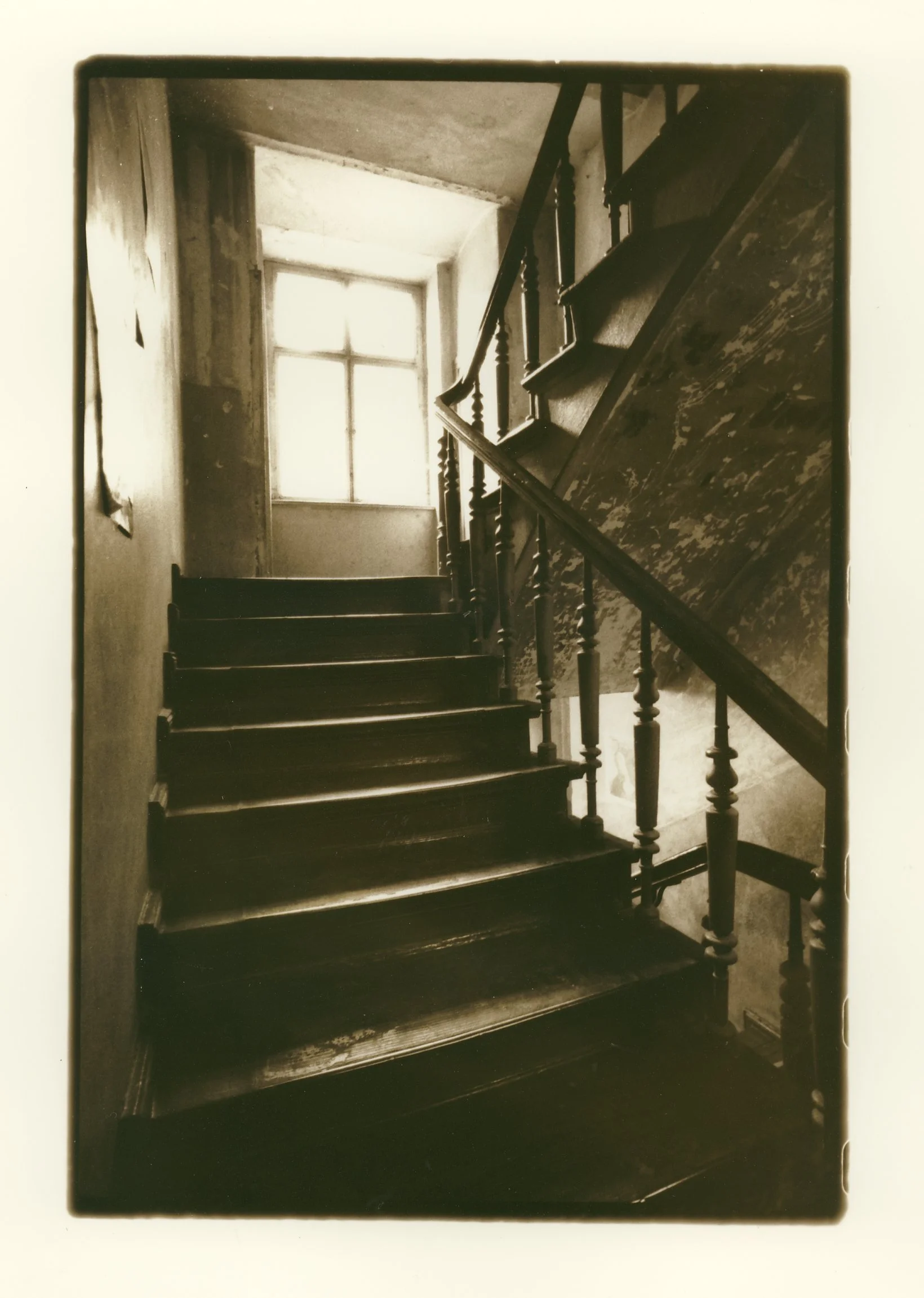 Old wooden staircase inside an aged building, with a window at the top allowing light to illuminate the stairs.