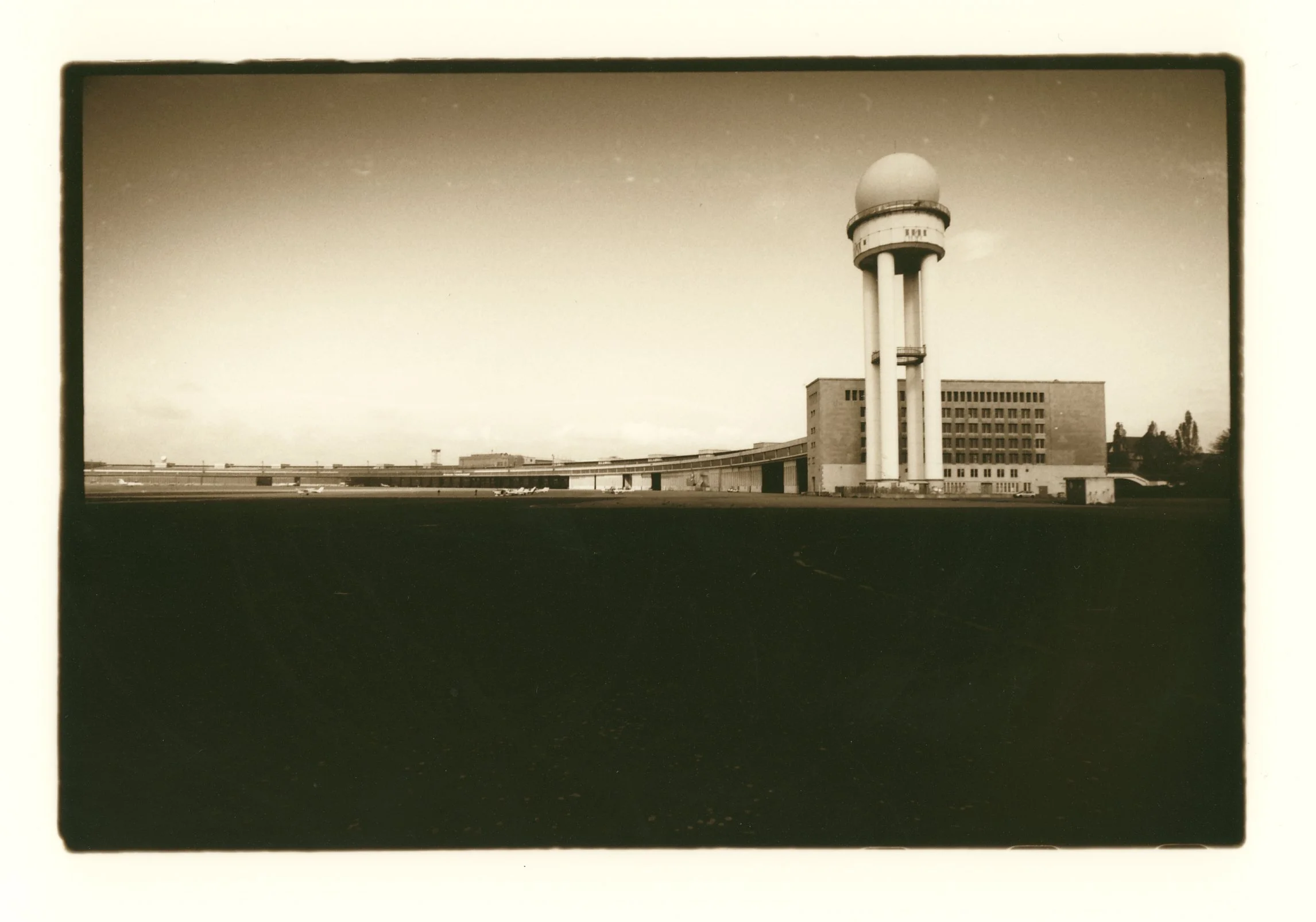 Black and white photo of a large building with a tall water tower with a spherical top, located on a flat open area.