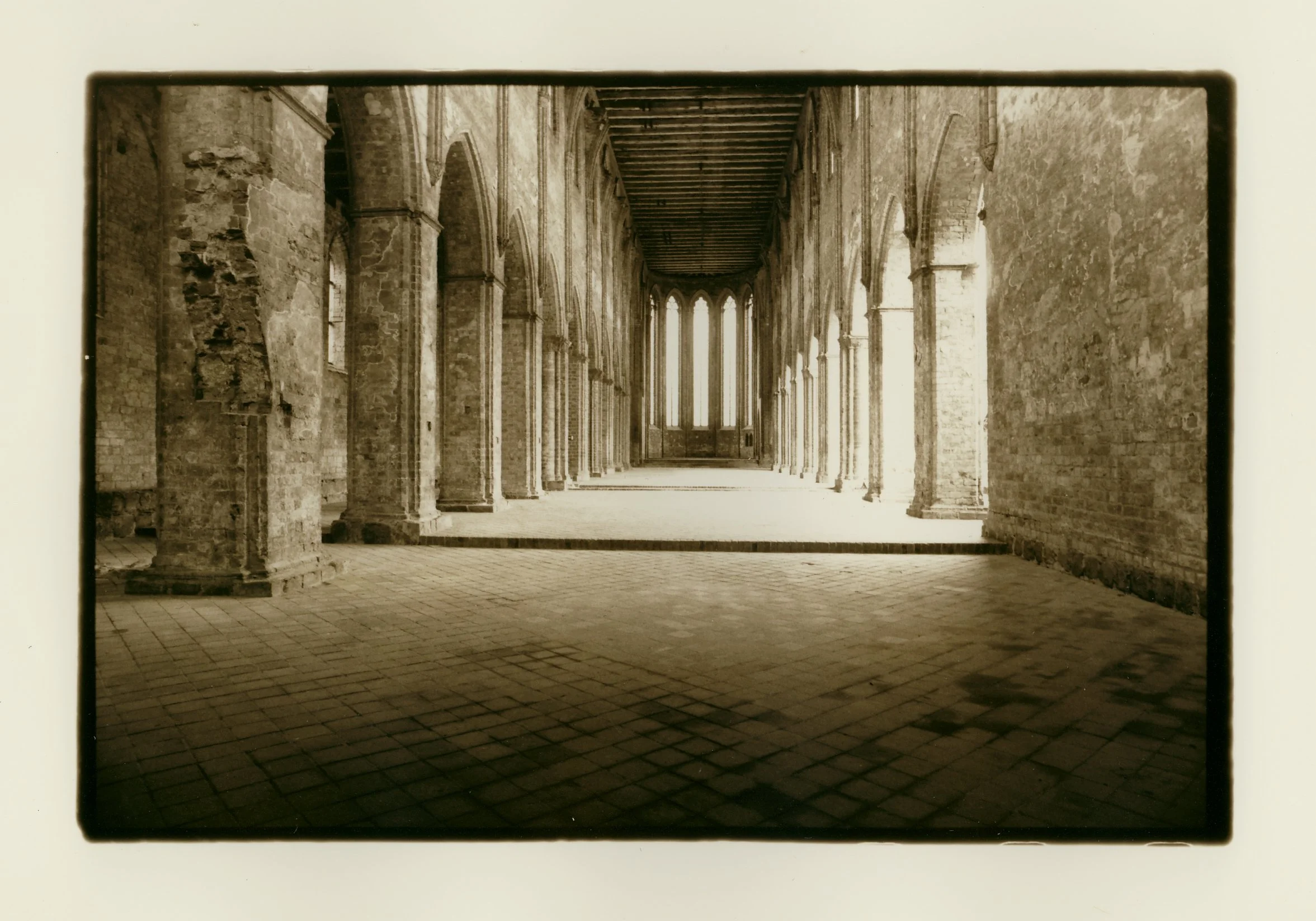 Sepia-toned interior of an old cathedral or church with tall brick columns, arched windows, and a brick floor.