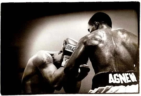 Two boxers in a match, one with gloves marked Everlast and the other with gloves marked Asey, engaging in close combat with sweaty skin visible.