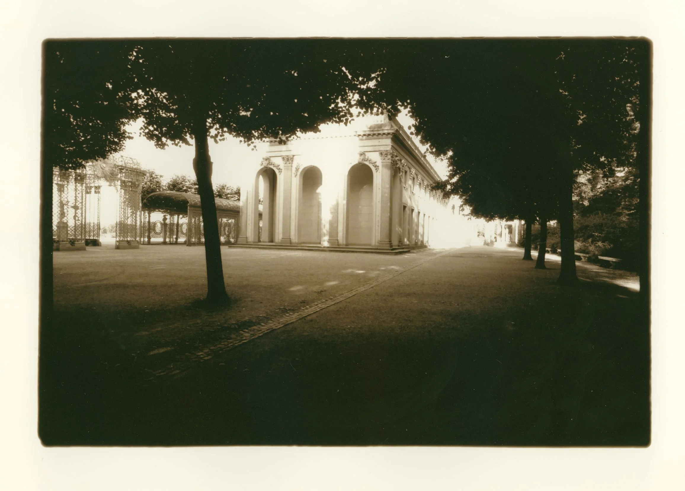 A sepia-toned photograph of a historic building with large arches, surrounded by trees, and a pathway leading up to it.