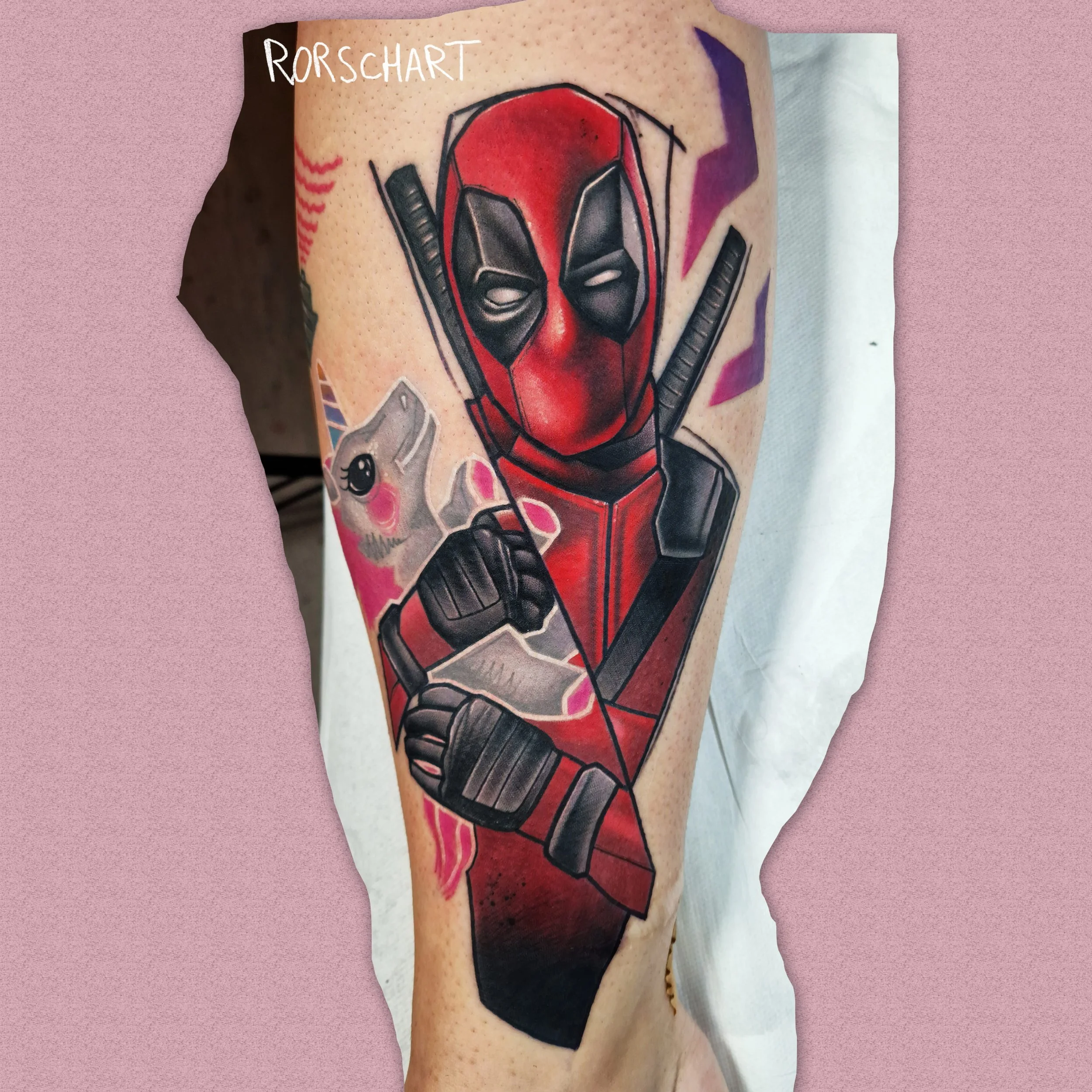 L'image montre un tatouage de Deadpool qui porte une peluche licorne. Le style graphique est contemporain, légèrement déstructuré et très coloré. Le tatouage a été réalisé par Rorschart, tatoueur à Nancy.