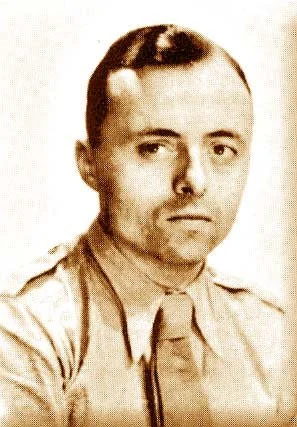 Portrait en noir et blanc d'un homme jeune avec des cheveux courts, portant une chemise militaire.
