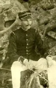 Jeune homme en uniforme militaire assis, fond forestier, photographie ancienne en sépia.