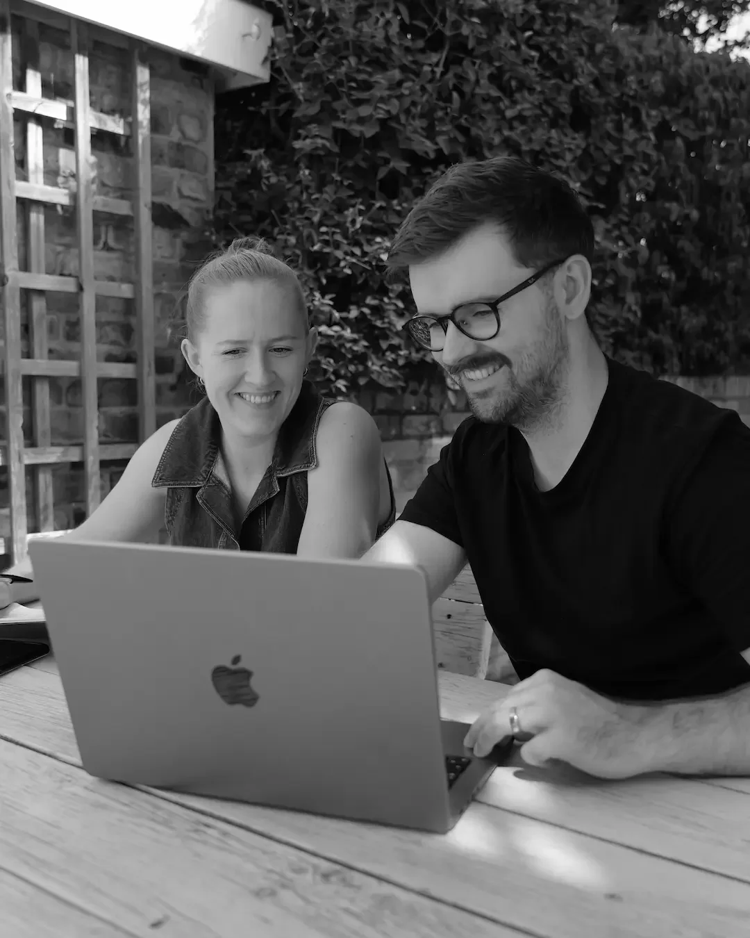 Black and white photo of two people sat in front of a laptop smiling