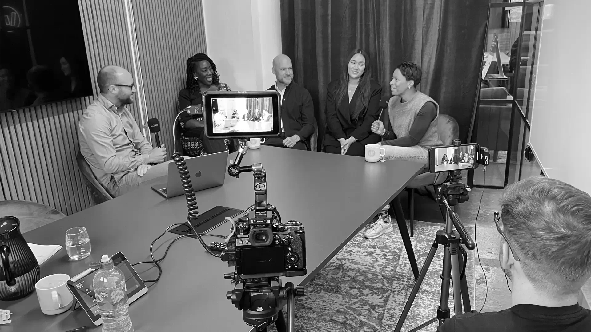 People gathered in an office being filmed for a podcast episode