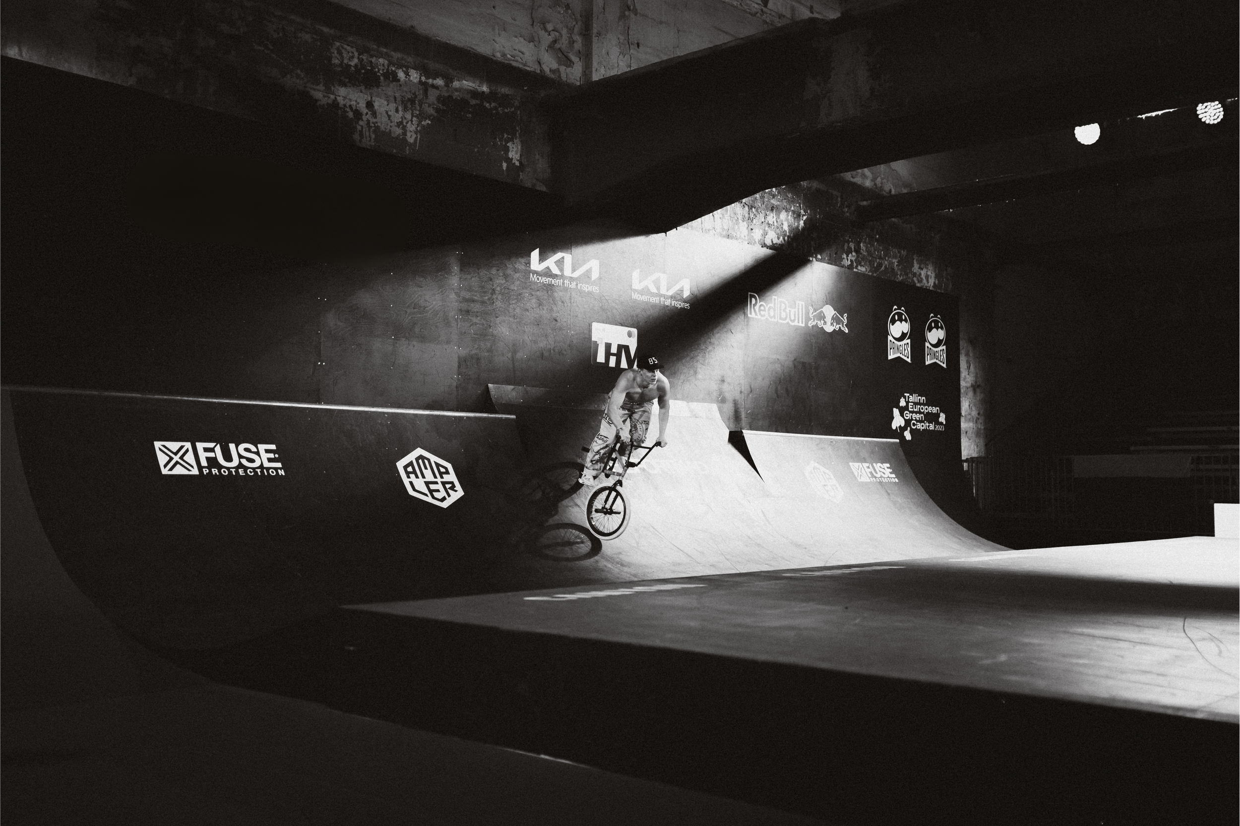 A person riding a BMX bike on a skatepark ramp with logos in black and white.