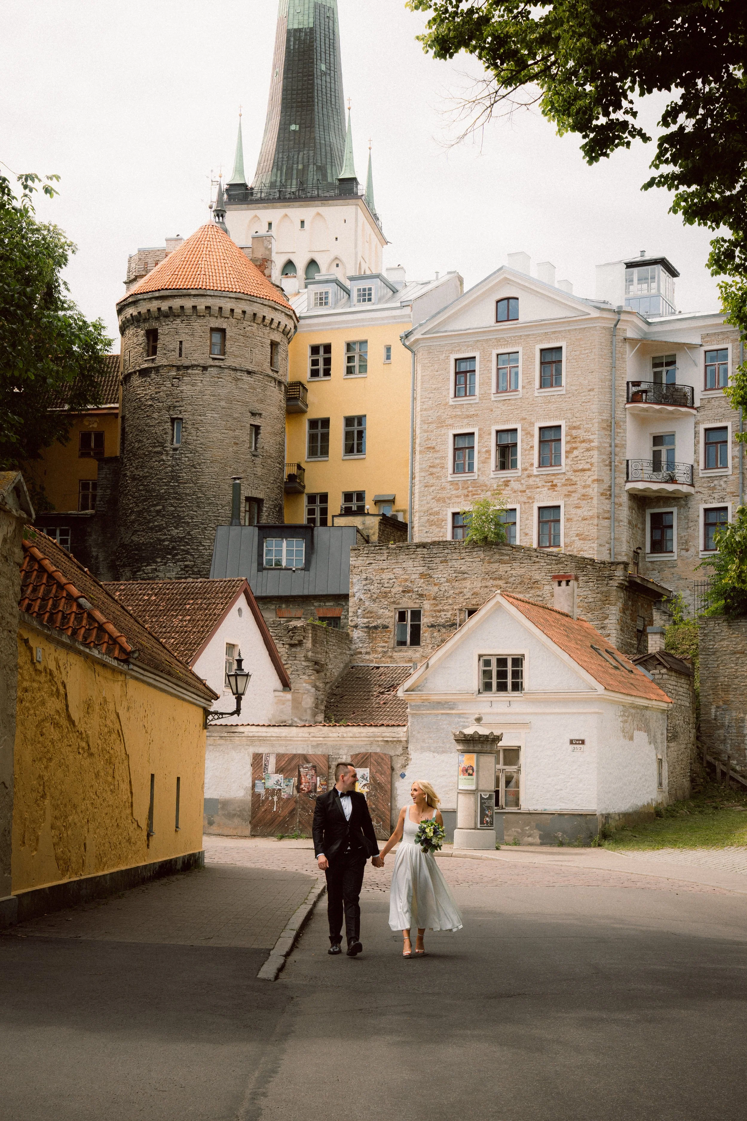 A wedding photo of a married couple in wedding dress and suit who are walking on an old town street hand-in-hand
