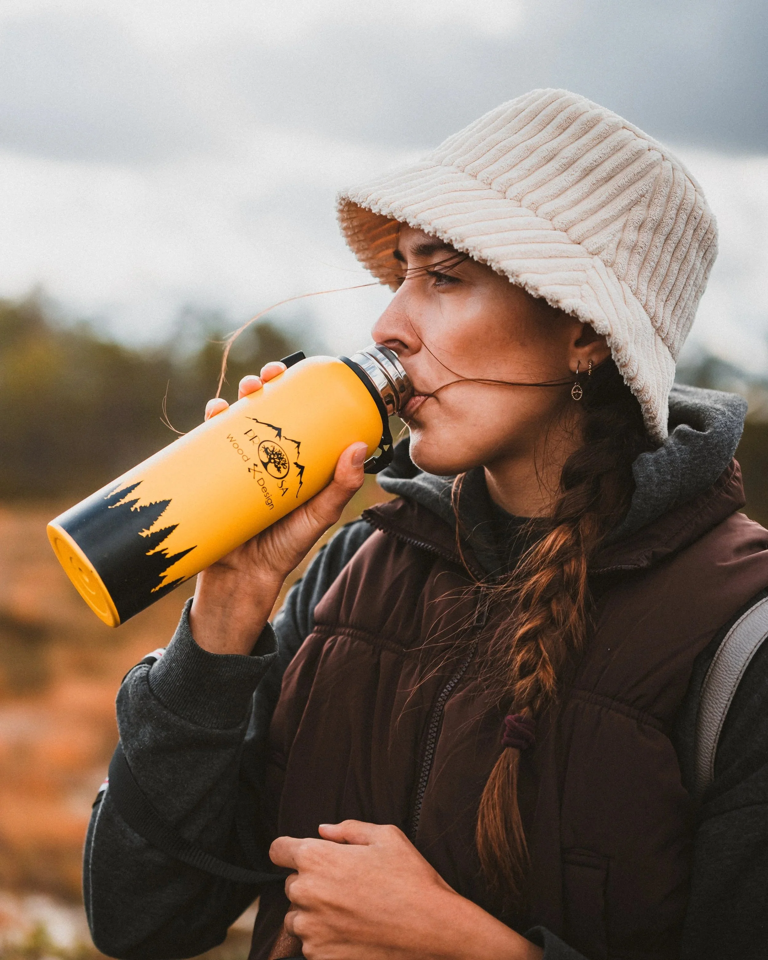 A photo of a girl drinking from Prosawood bottle outdoors in nature