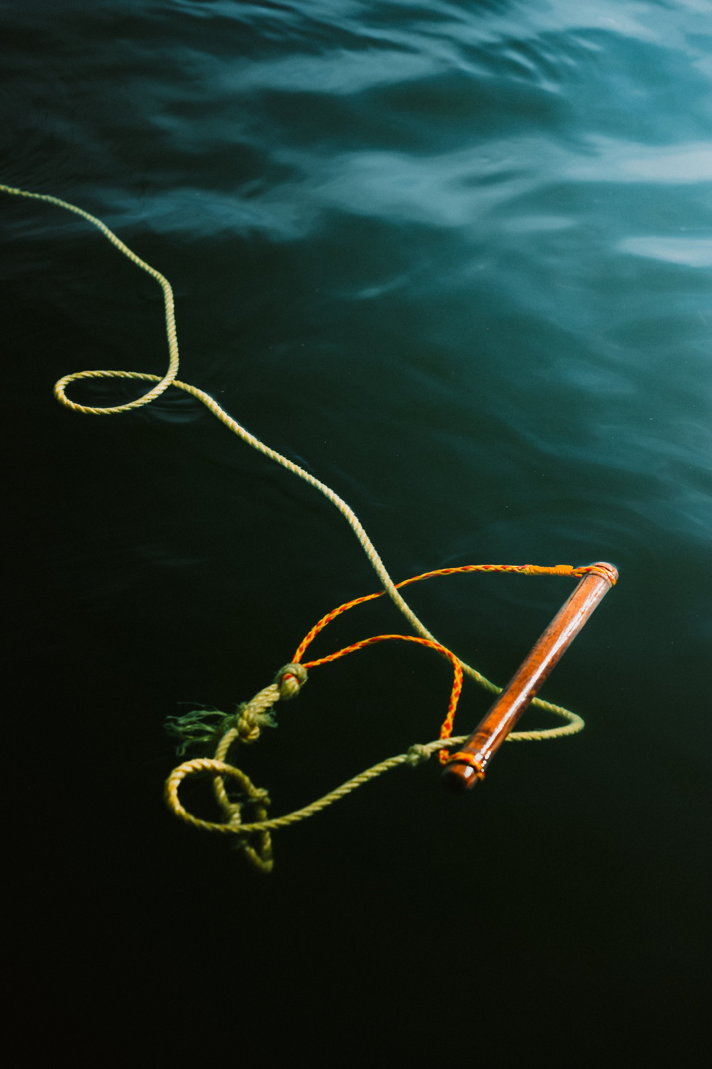 A wooden floating object connected to green and orange ropes on a dark water surface.