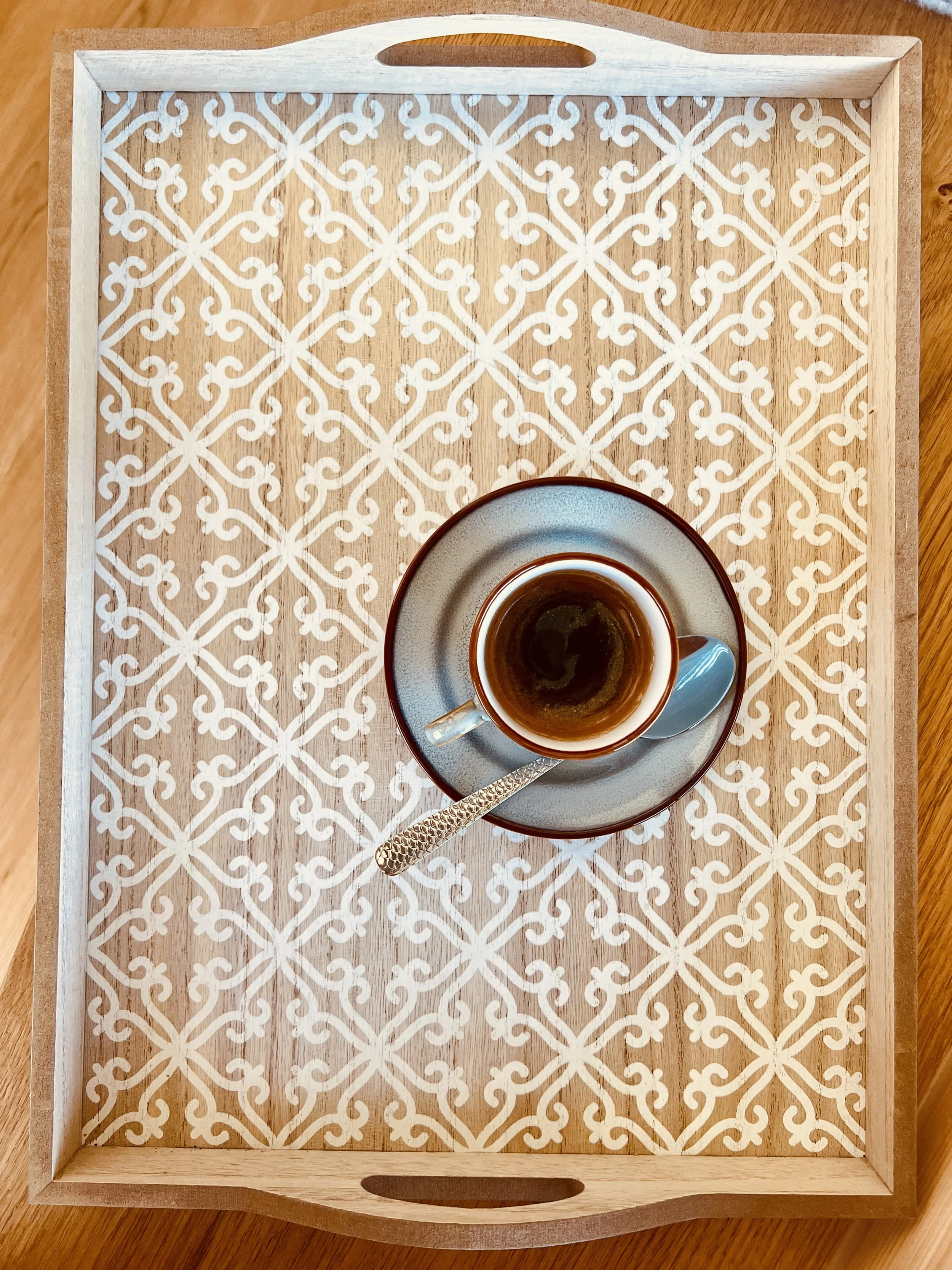 Ein Holztablett mit weißem Muster und einem weißen Kaffeetassen mit schwarzem Kaffee darin, auf einem Holzoberfläche.