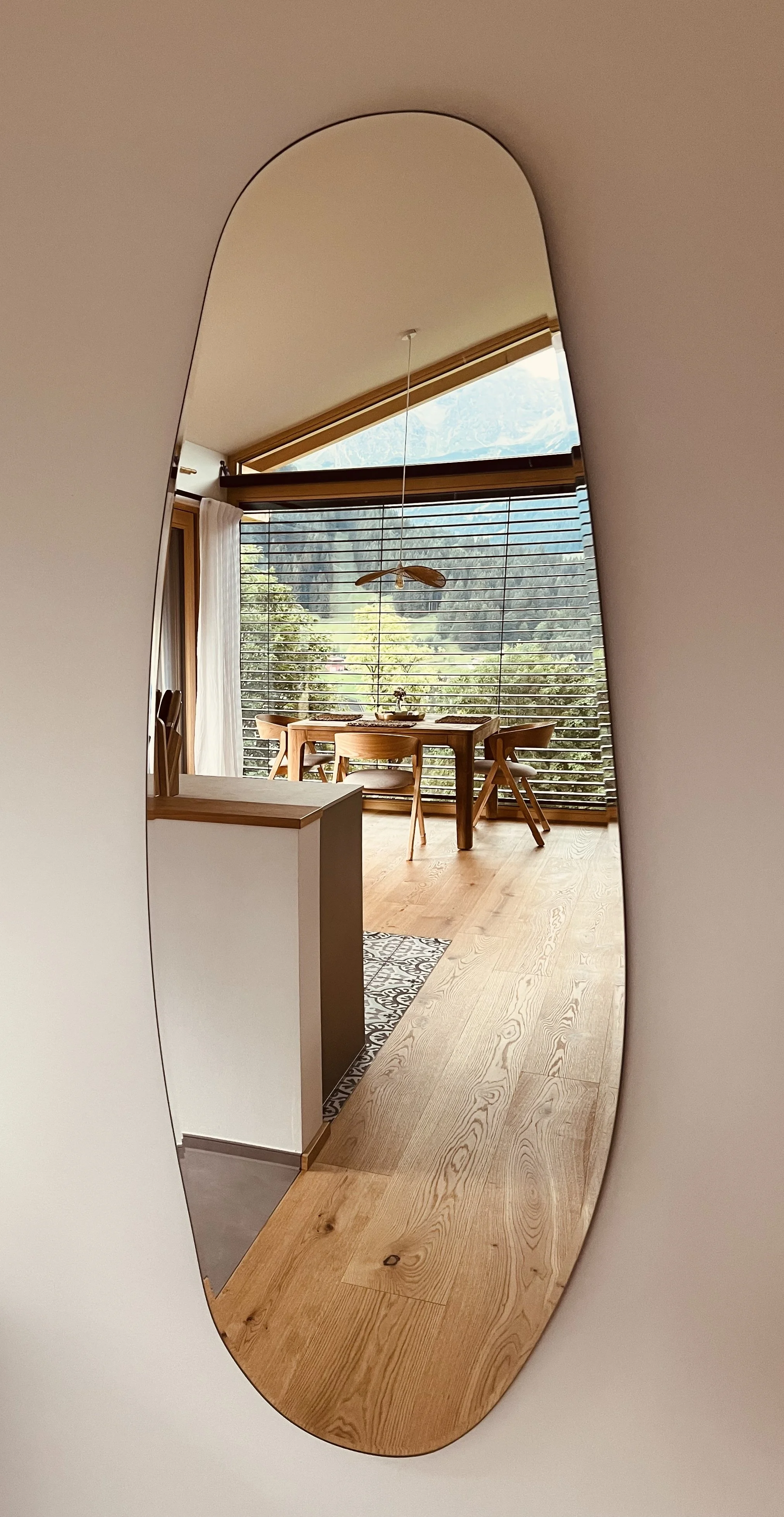 Helle Wohnküche mit großen Fenstern, Holztisch und Stühlen, Blick ins Grünen, Deckenventilator, von einer ovalen Spiegel reflexartig sichtbar