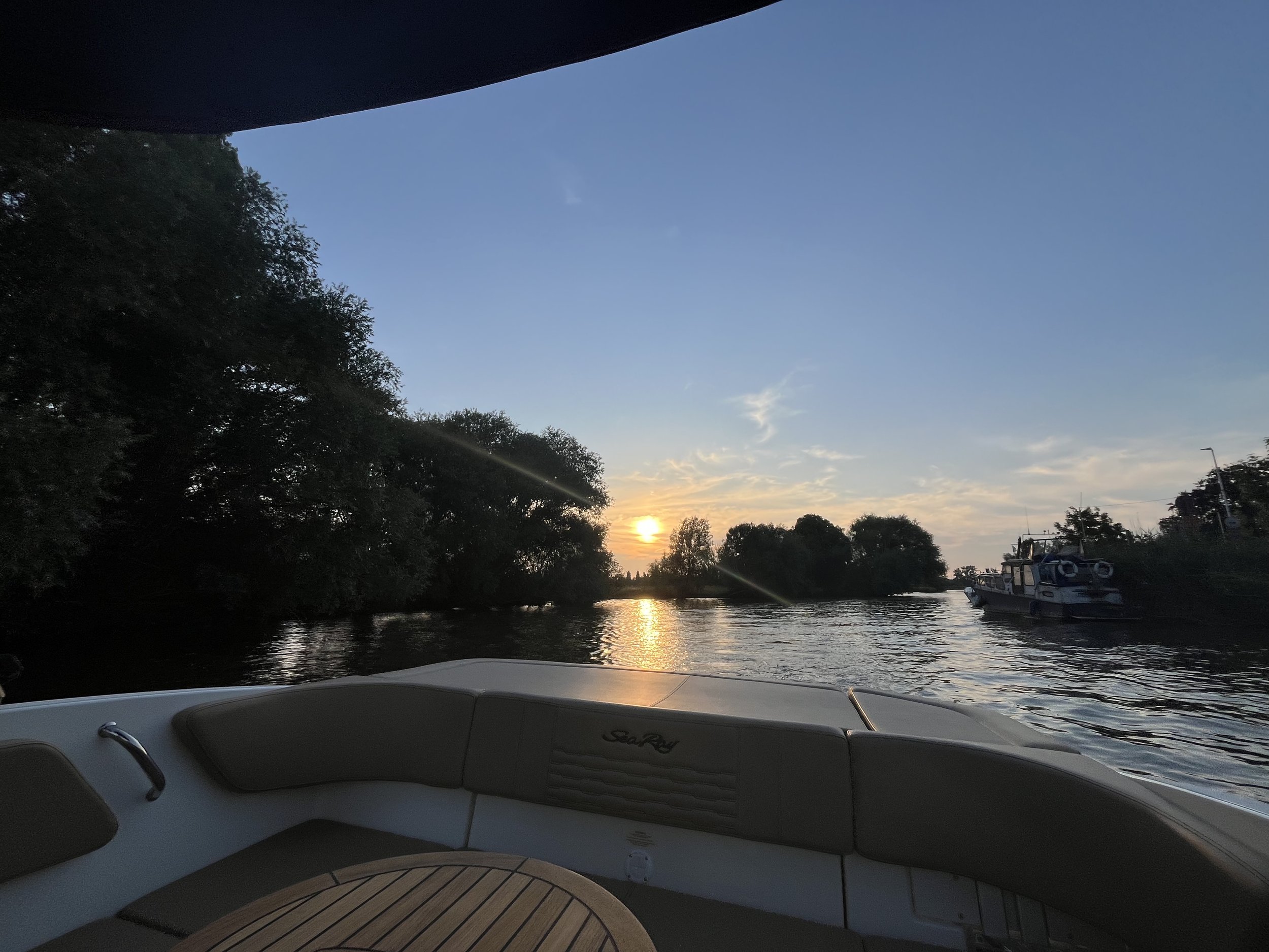 Een boot op het water bij zonsondergang met bomen langs de oevers en een ander bootje in de verte.
