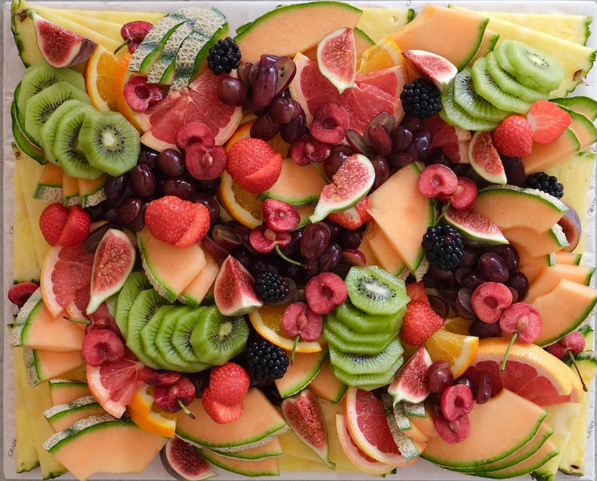 Een kleurrijk assortiment gesneden vers fruit, waaronder kiwi, watermeloen, ananas, grapefruit, aardbeien, blauwe bessen, bramen, kers, druiven, vijg en sinaasappel.