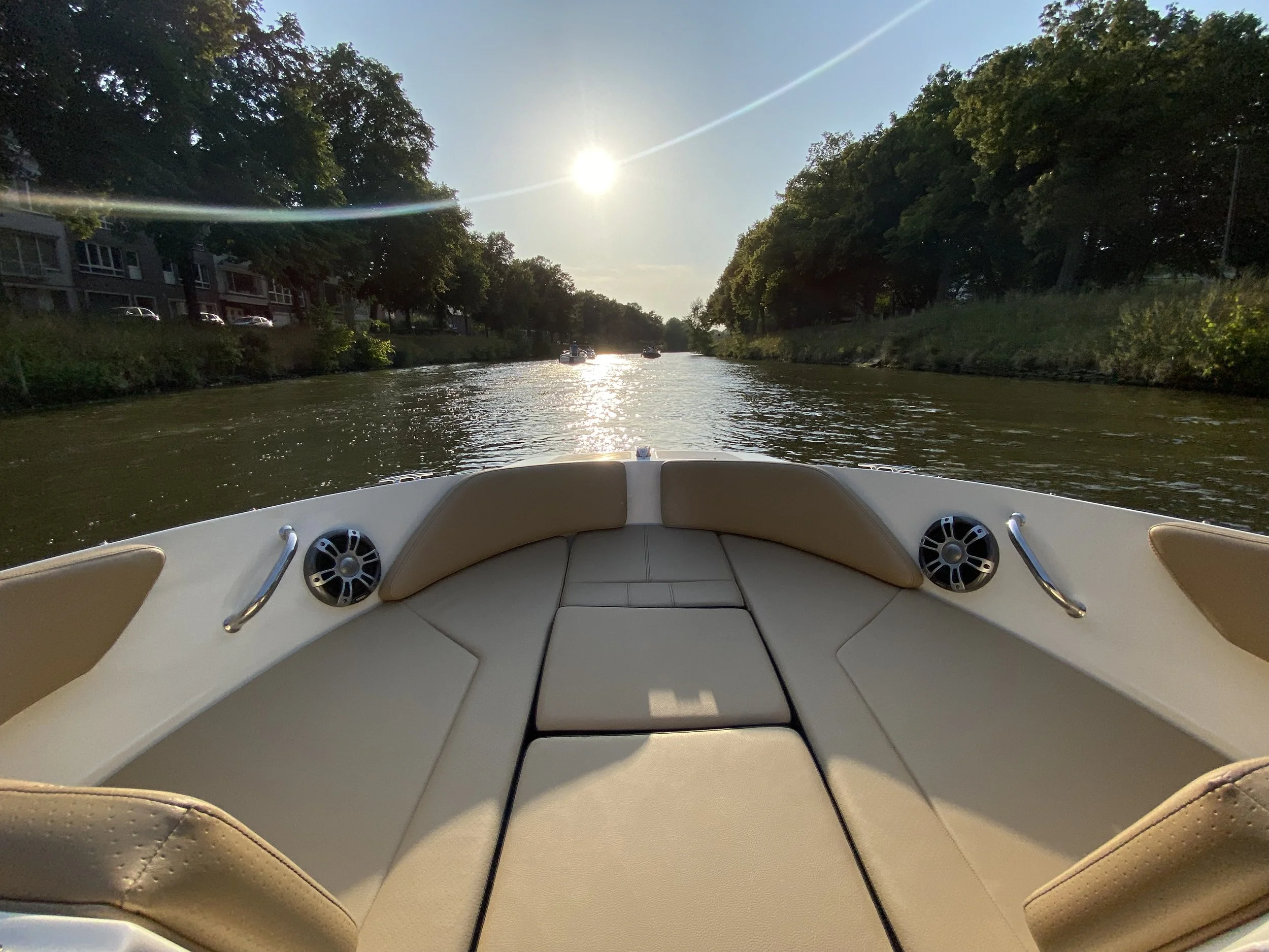 Foto van een boot op een rivier met de zon die schijnt en bomen langs de oever.