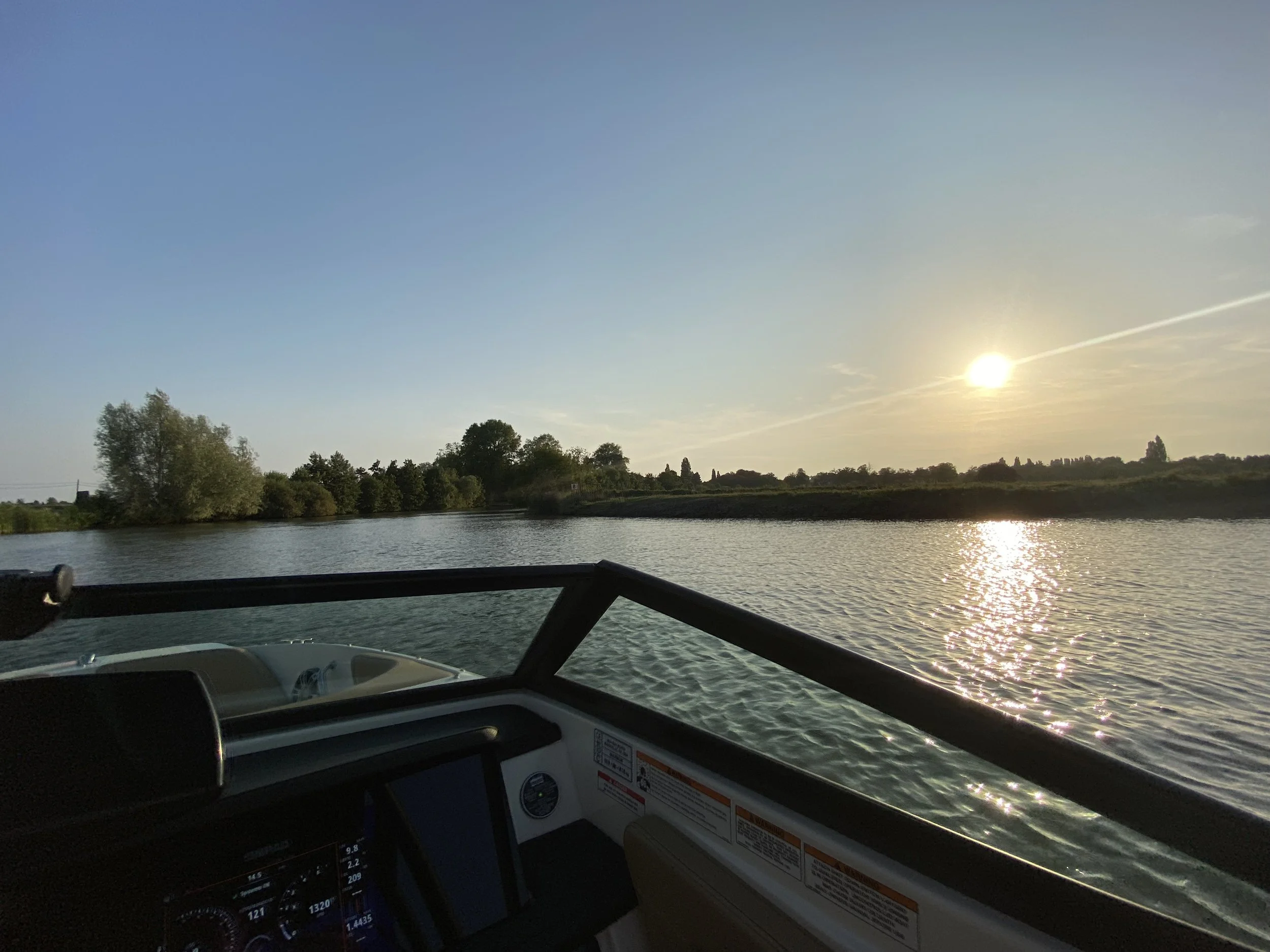 Uitzicht vanaf een boot met navigatiescherm over een rivier tijdens zonsondergang.