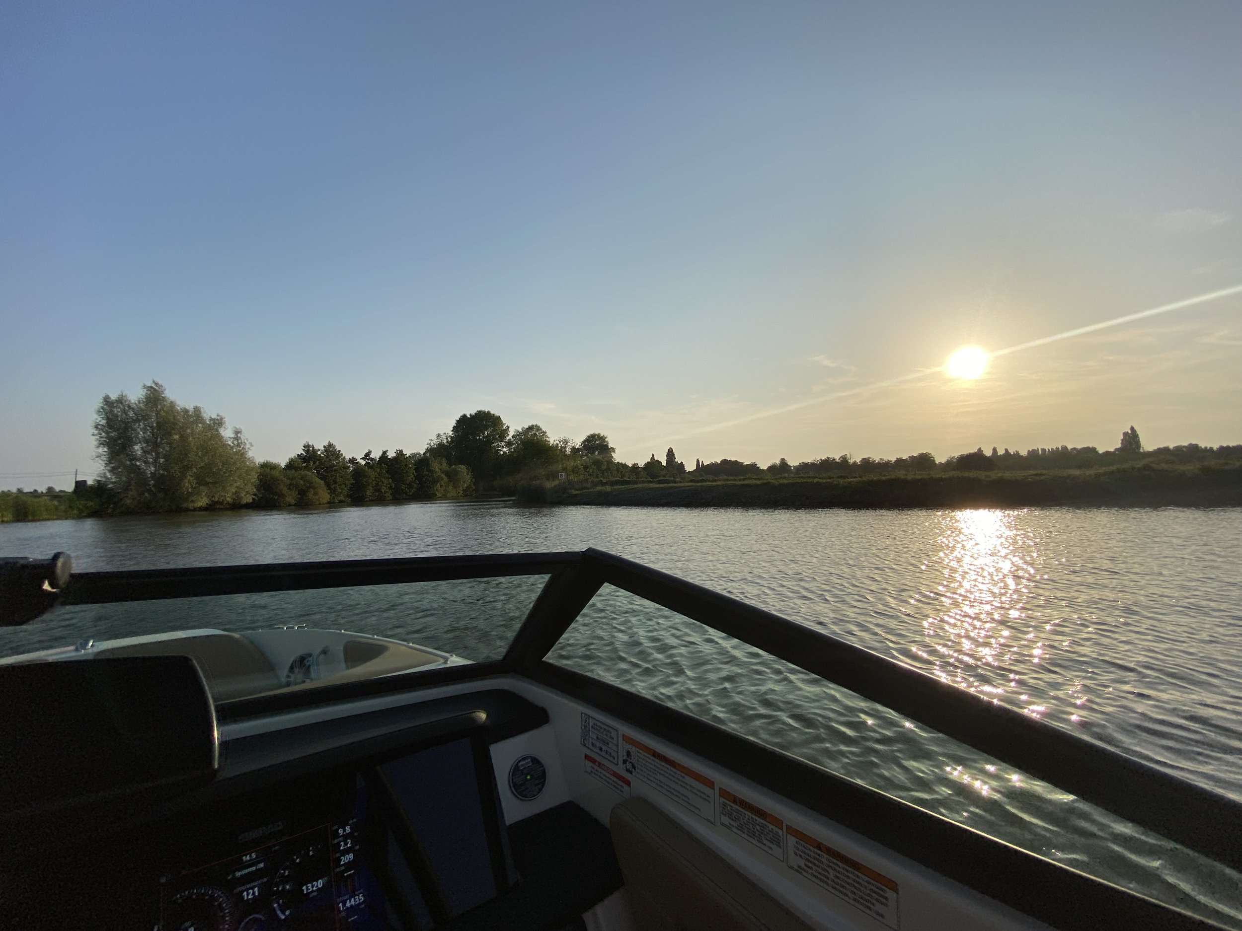 Uitzicht vanaf een boot met navigatiescherm over een rivier tijdens zonsondergang.